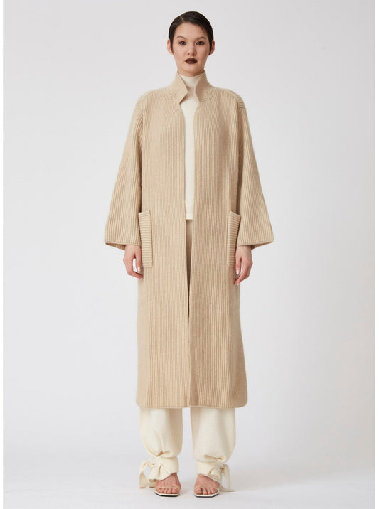 Front view of model wearing a beige Midi cardigan coat in ribbed cashmere knit. Straight cut with a relaxed fit, deep patch pockets and generous sleeves which can be rolled back.