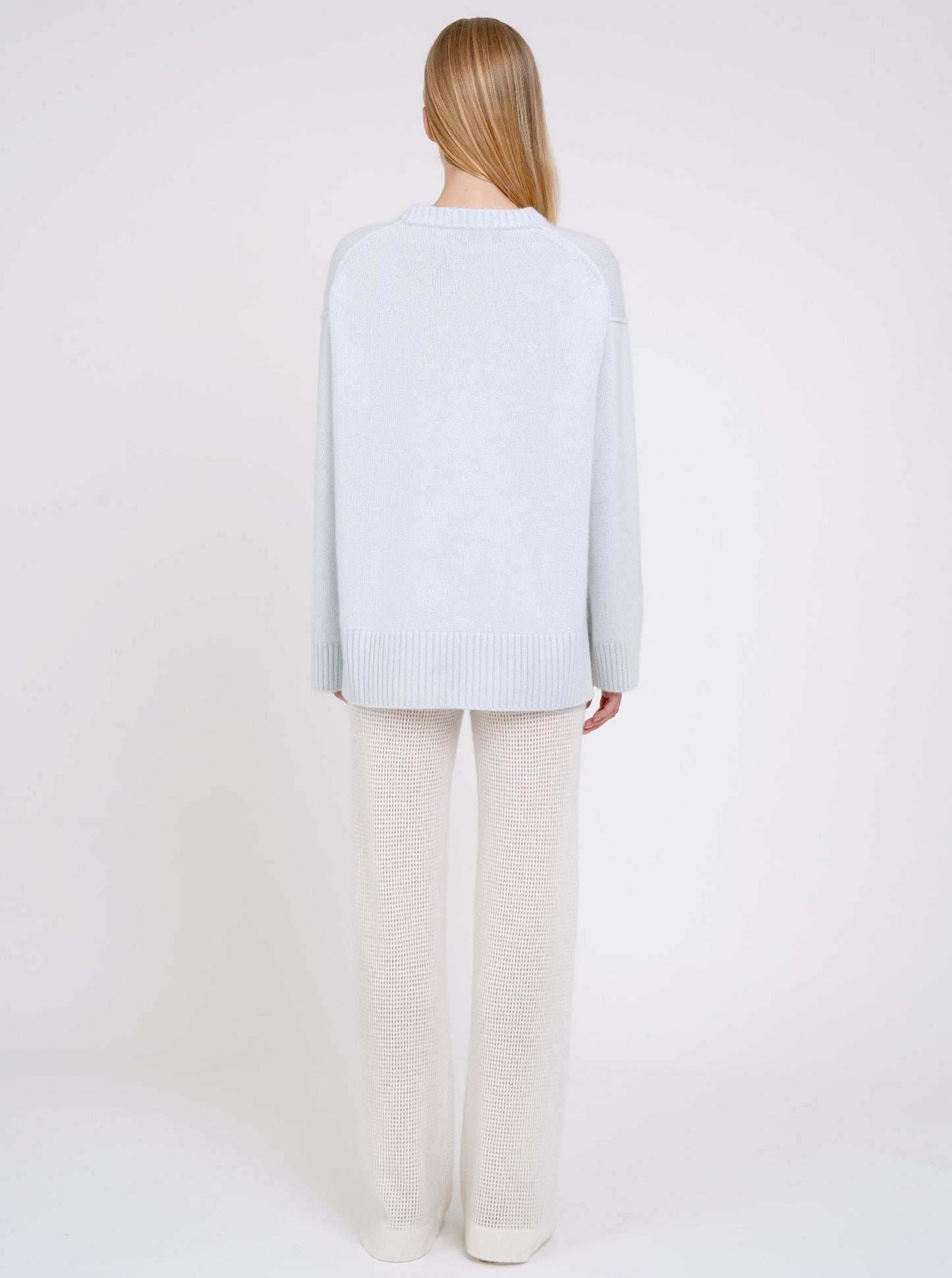 Back view model in light blue long jumper with round neck, long sleeves and white cashmere knit pants.