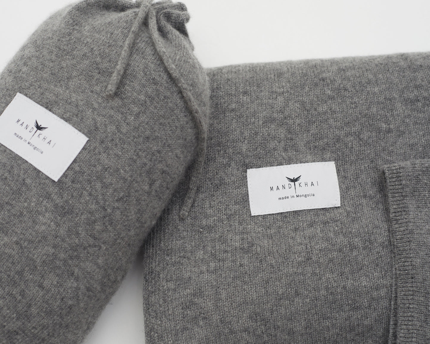 Close up flat lay of the Grey Cashmere Shawl With Travel Pouch featuring Mandkhai's label and the side of the travel pouch