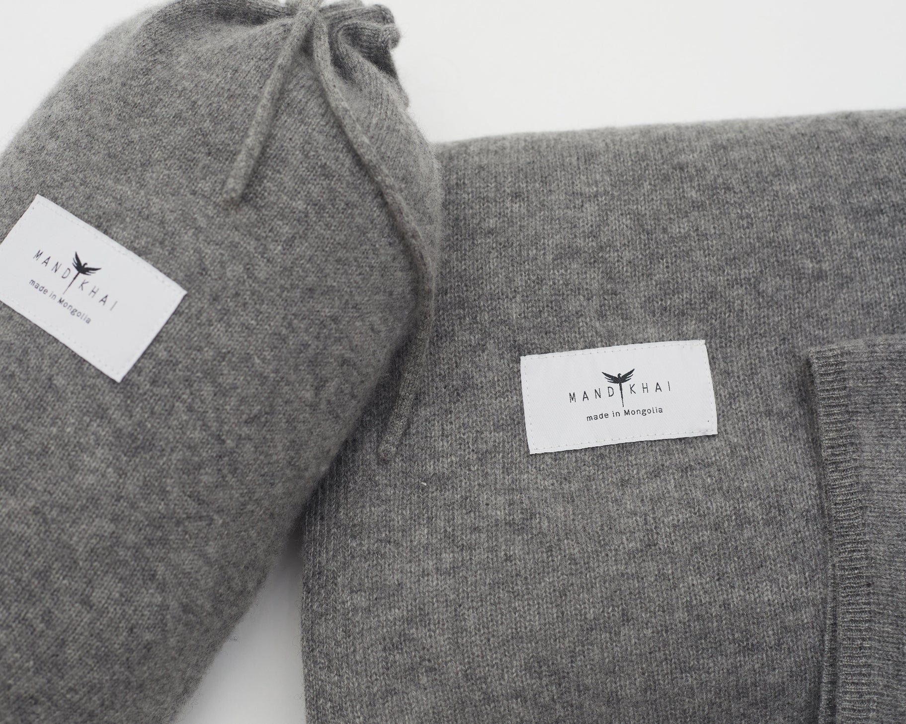 Close up flat lay of the Grey Cashmere Shawl With Travel Pouch featuring Mandkhai's label and the side of the travel pouch