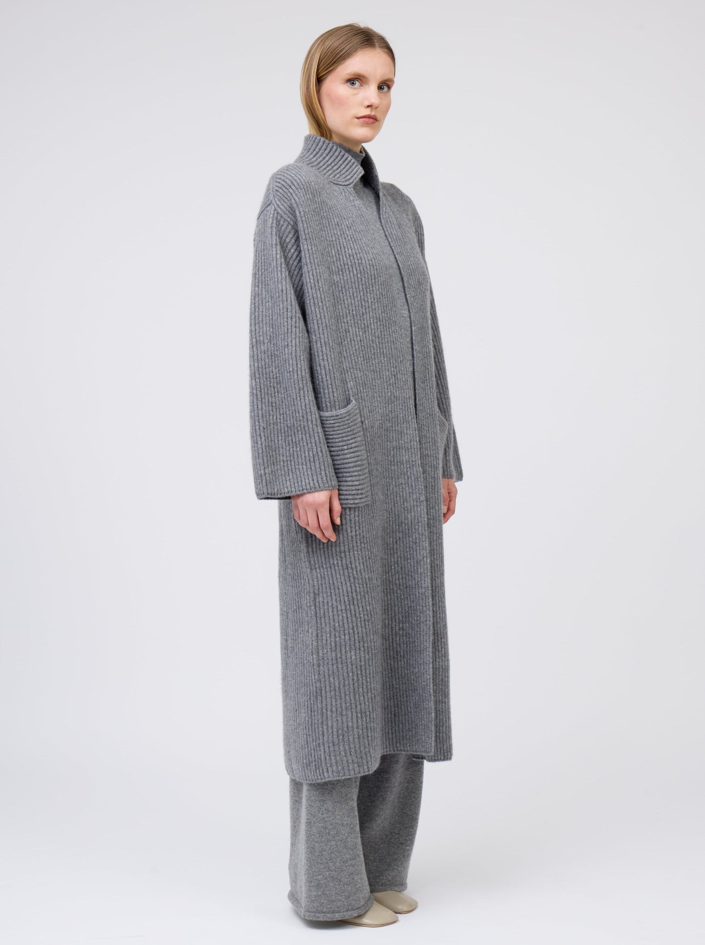 Model wearing a long grey cardigan coat in ribbed knit. Straight cut with a relaxed fit, deep patch pockets and generous long sleeves.