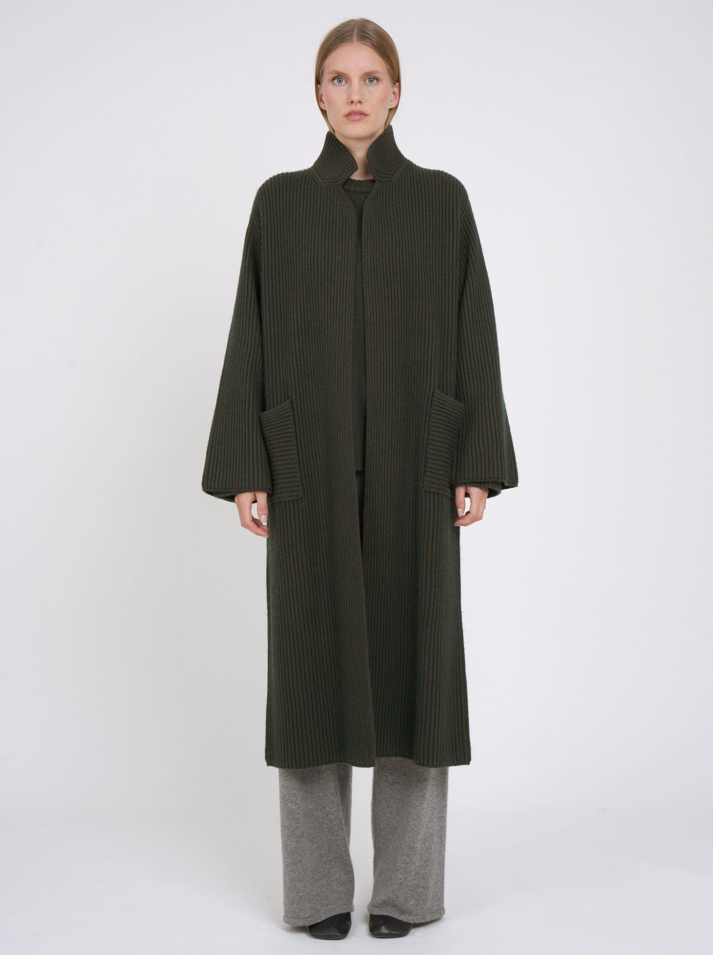 Model wearing a long khaki green cardigan coat in ribbed knit cashmere. Straight cut with a relaxed fit, high collar, patch pockets and generous long sleeves.
