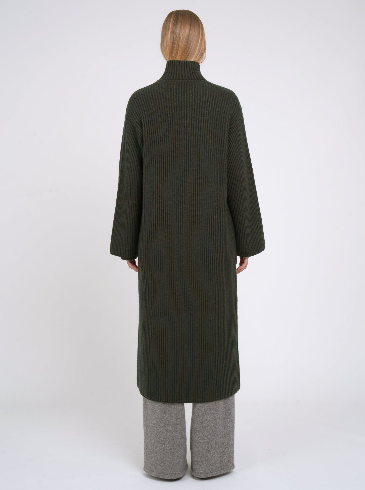 Back of model wearing a long khaki green cardigan coat in ribbed knit cashmere; worn with grey cashmere pants.