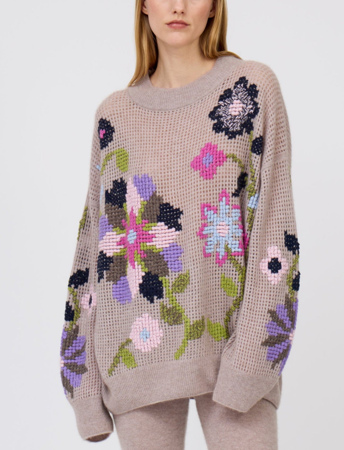 Close up of light weight, beige cashmere, net knit jumper, with round neck, long sleeves and multi-coloured, cross-stitch, floral, hand embroidery.