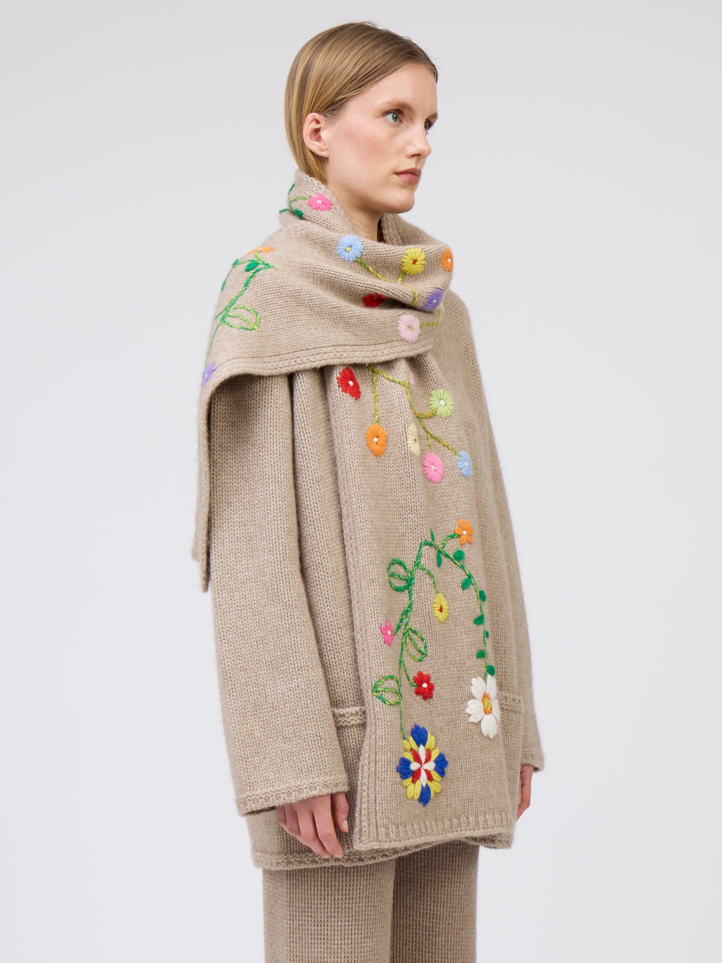 Close-up, side view model wearing light brown cashmere hip-length jacket with brightly coloured floral hand-embroidered scarf.