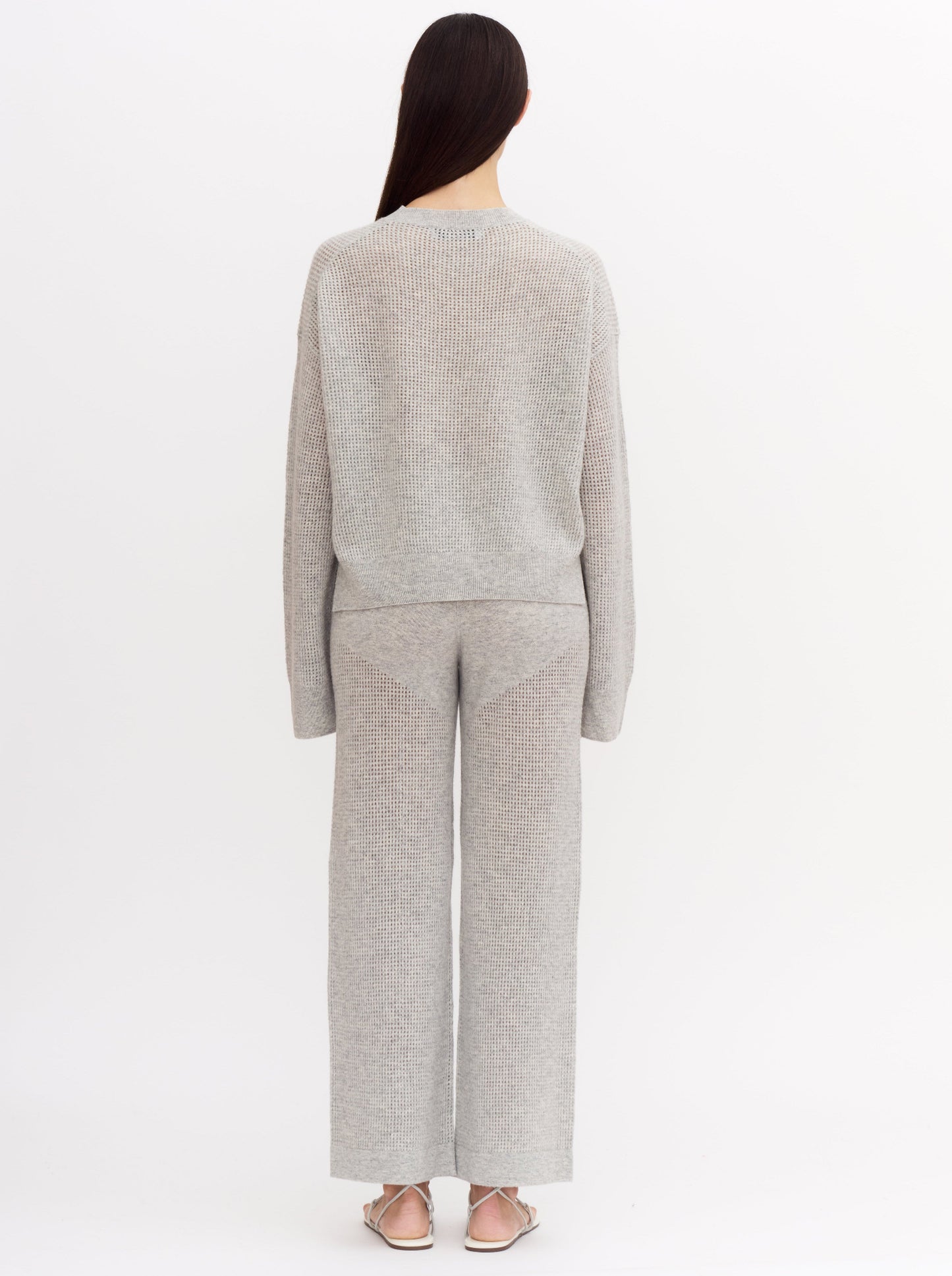 Back view of model wearing light grey cashmere net knit cashmere long sleeve sweater with wide leg matching light grey cashmere pants.