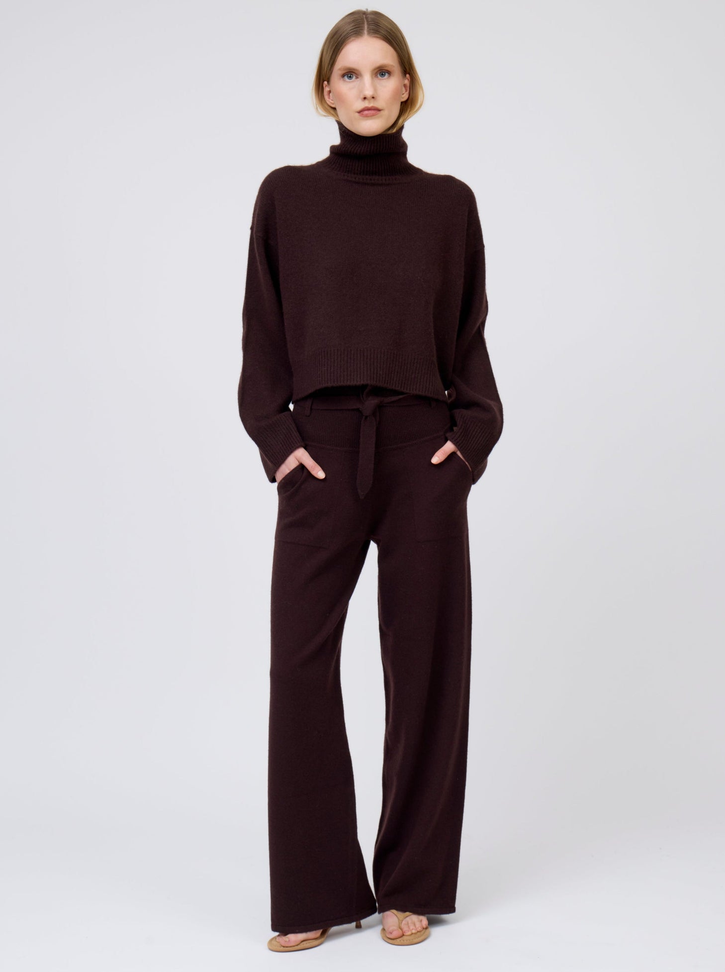 Model wears mahogany brown cashmere, wide leg pants with tie belt and pockets; worn with matching mahogany brown  cashmere, cropped length, roll-neck sweater.