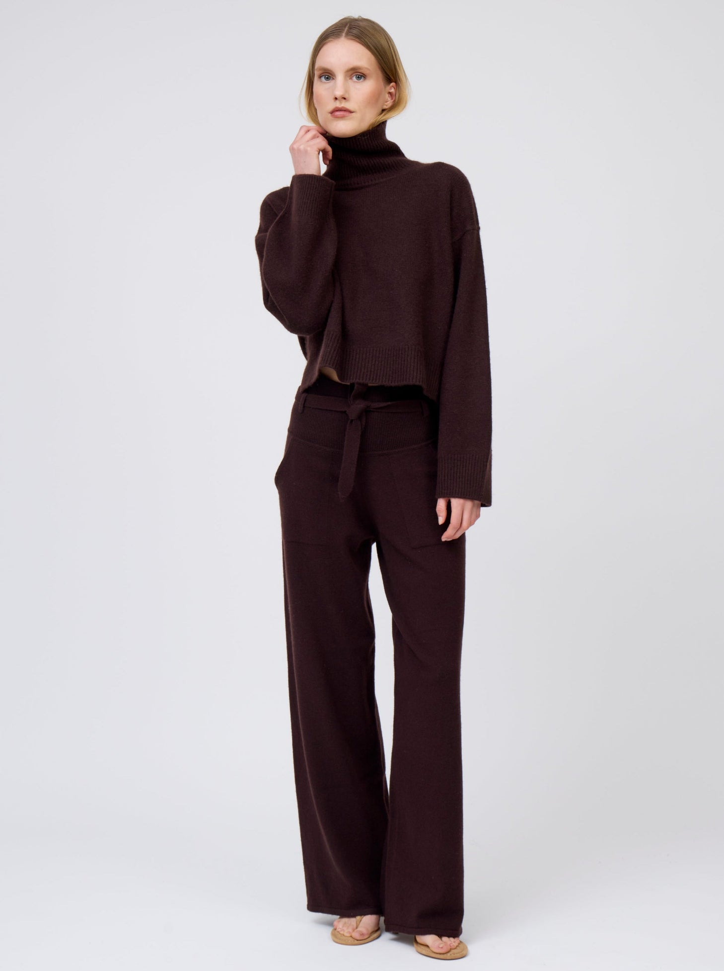 Model is wearing mahogany brown wide-leg cashmere pants with tie belt and side pockets; worn with matching mahogany brown  cashmere, cropped length, roll-neck jumper.