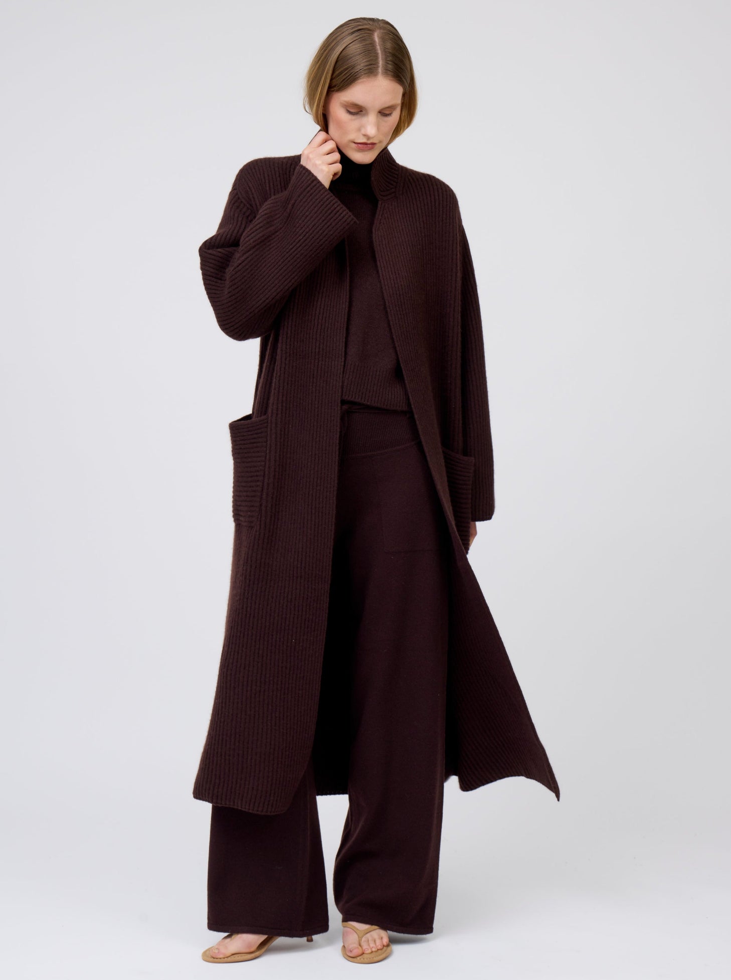 Model wears mahogany brown cashmere, wide leg pants with tie belt and pockets; worn under matching mahogany brown  cashmere, long-line ribbed knit coat with patch pockets.