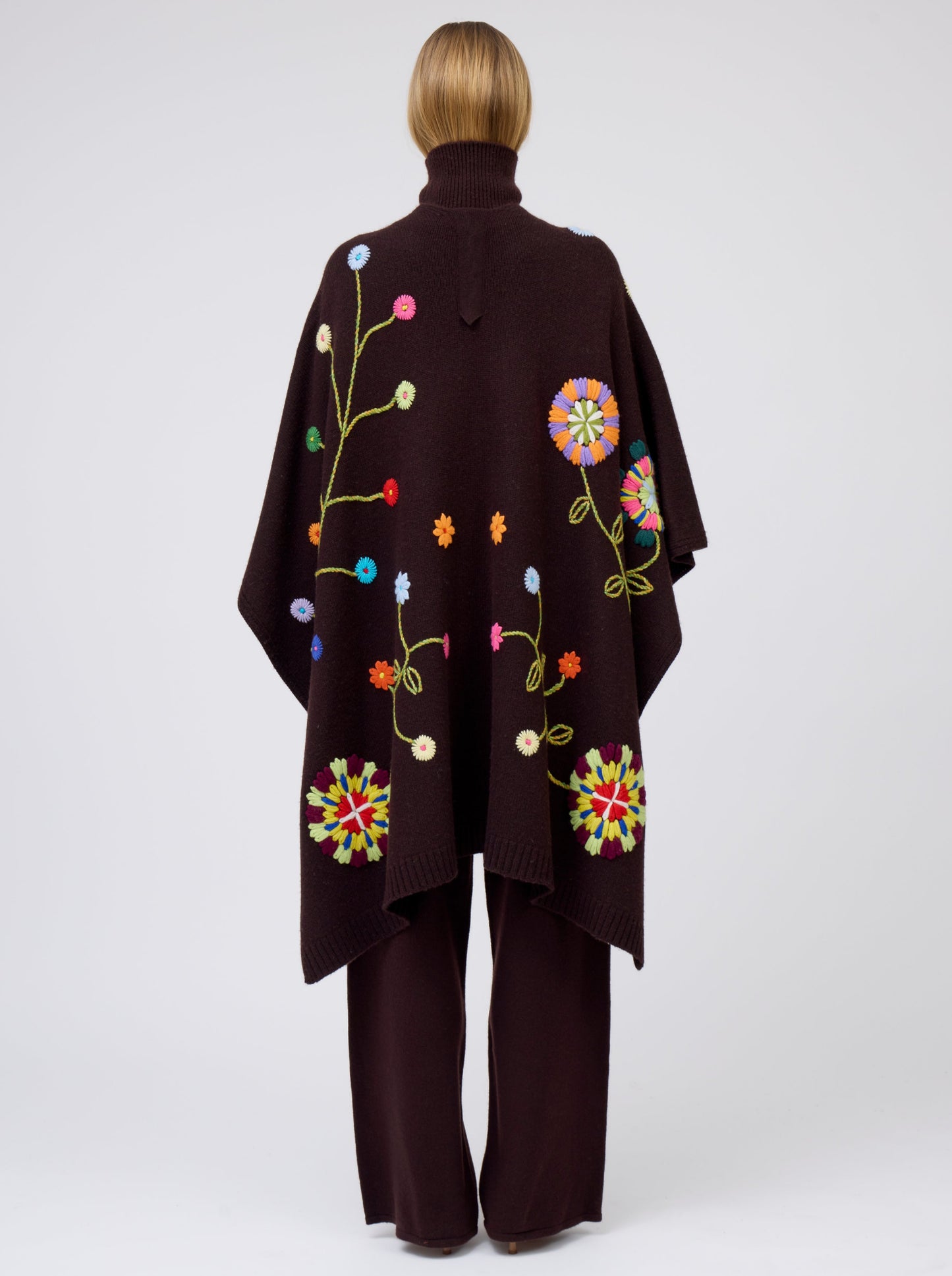 Back view model wearing mahogany brown cashmere mid-length wrap with brightly coloured hand-embroidery; worn with matching brown jumper and brown pants.
