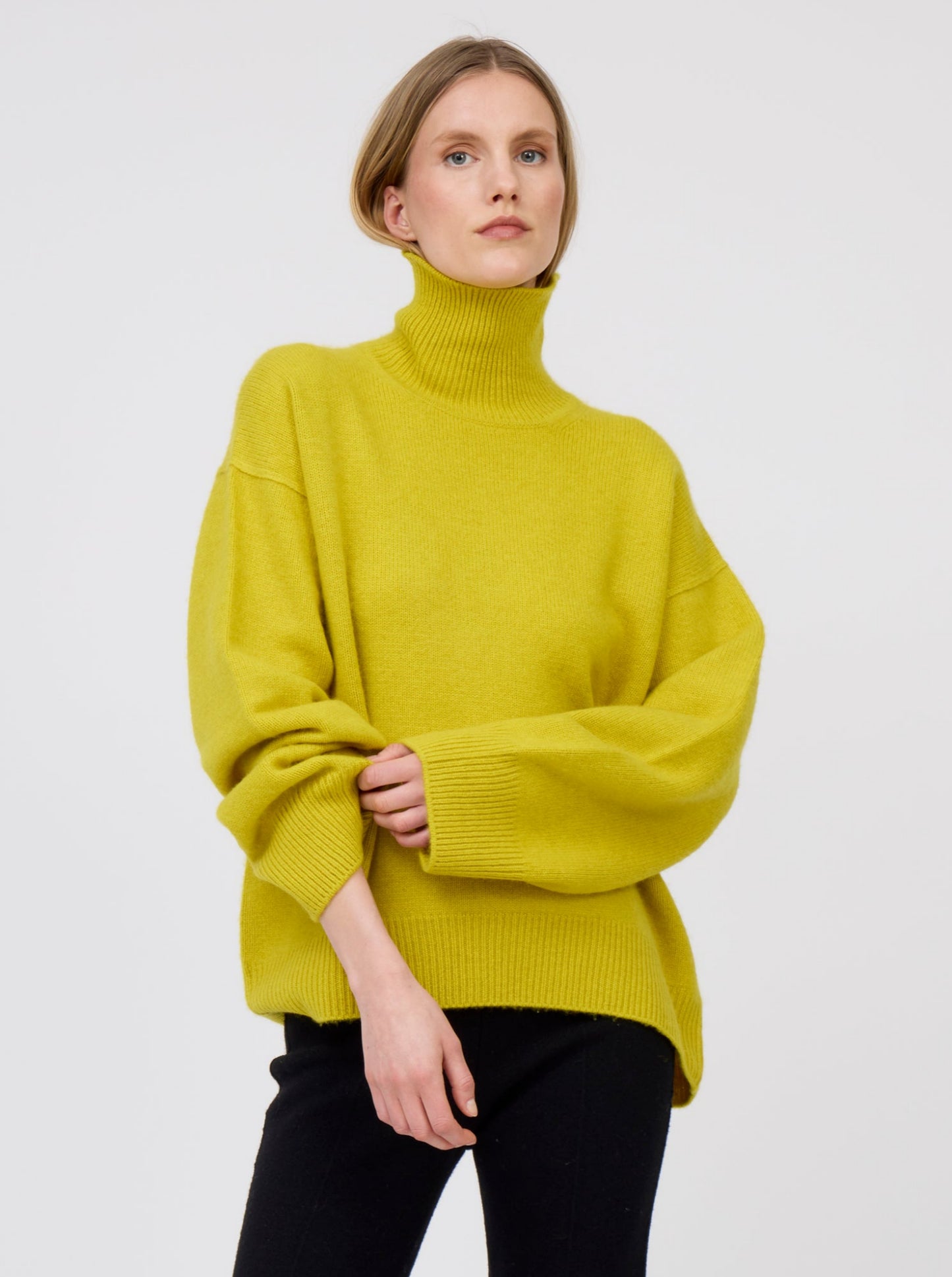 Cropped view model wears mustard yellow cashmere roll neck oversized jumper with black tailored cashmere pants.