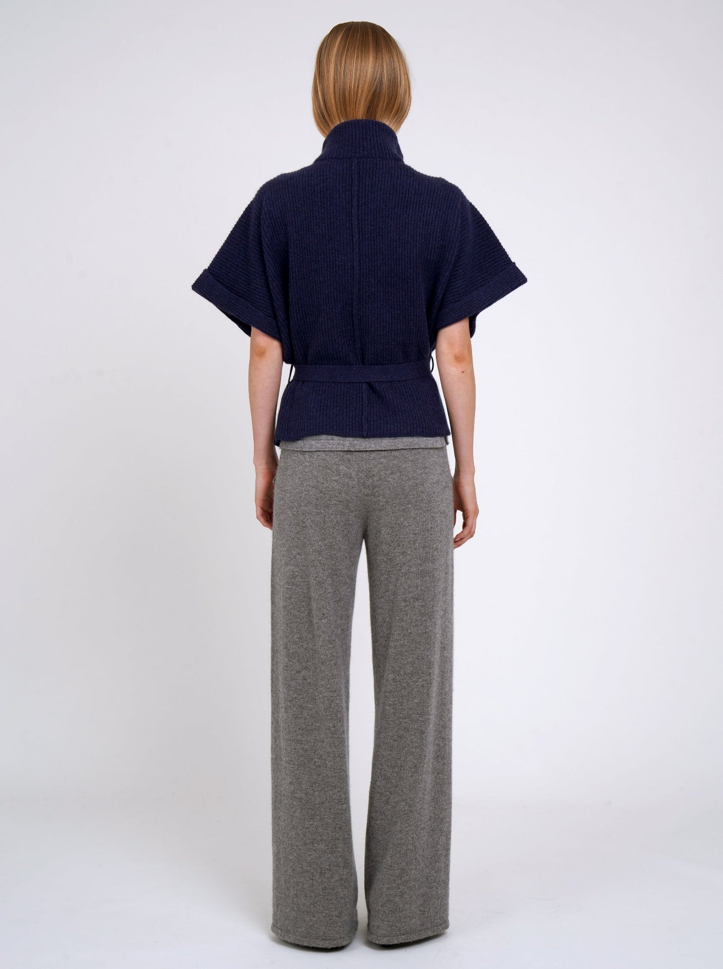 Back view model wears navy cashmere short ribbed knit jacket with grey wide leg pants.