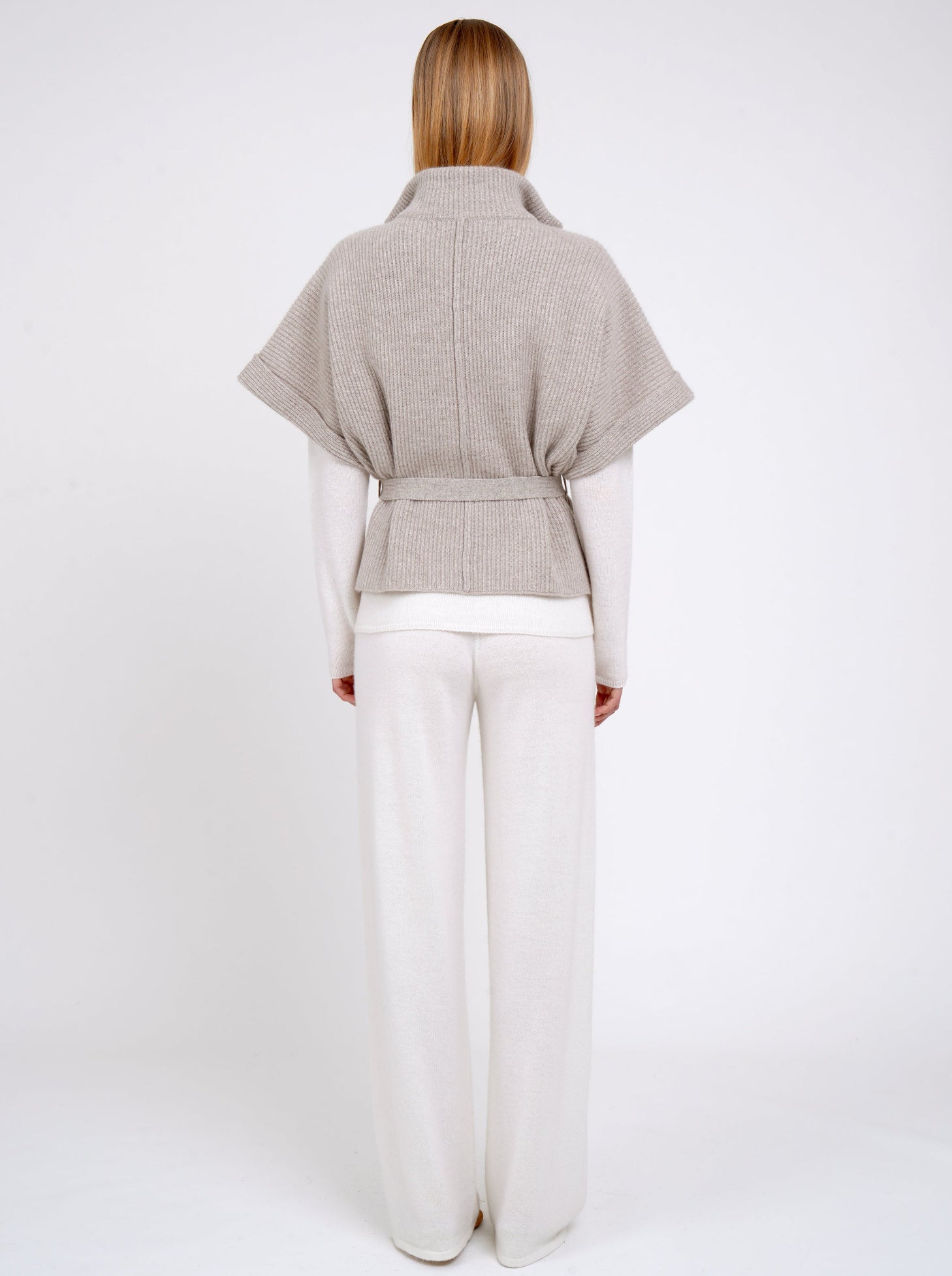 Back view model wears beige cashmere short ribbed knit jacket with white wide leg pants.