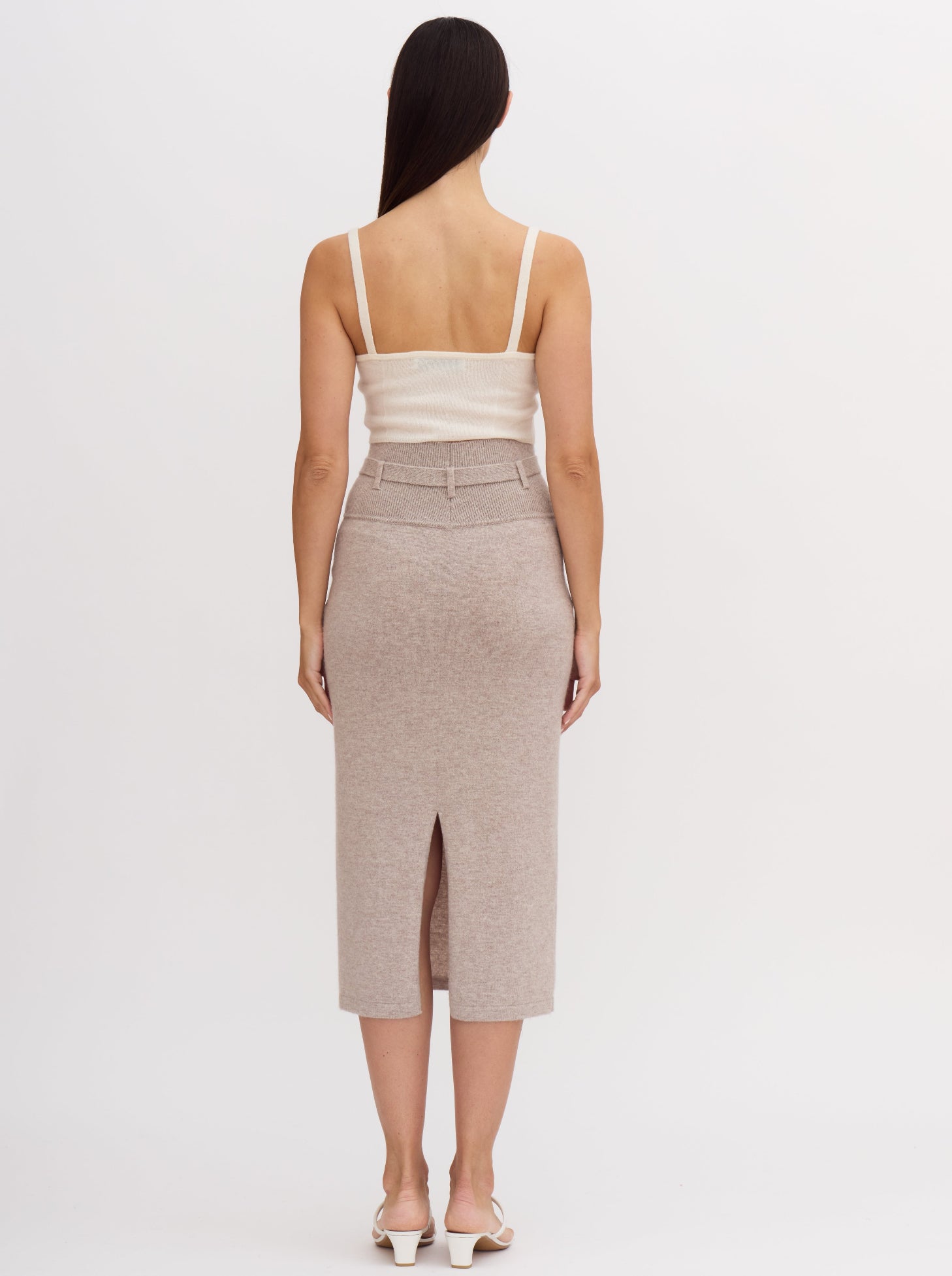 Back view of model wearing beige cashmere high waisted pencil skirt with tie belt and back slit.