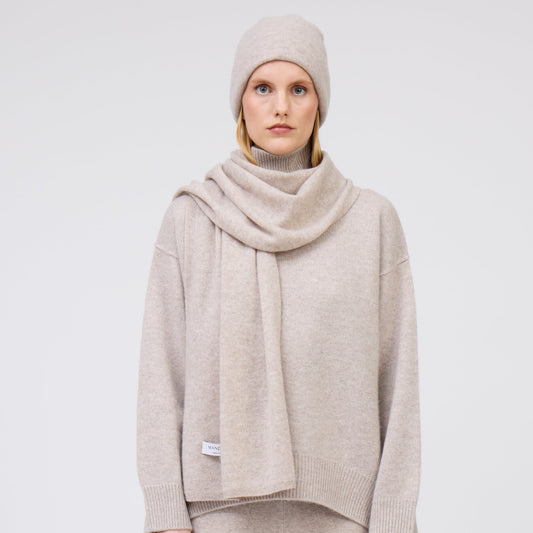 Front view of modal wearing pale beige cashmere scarf with matching beige beanie and cashmere jumper.