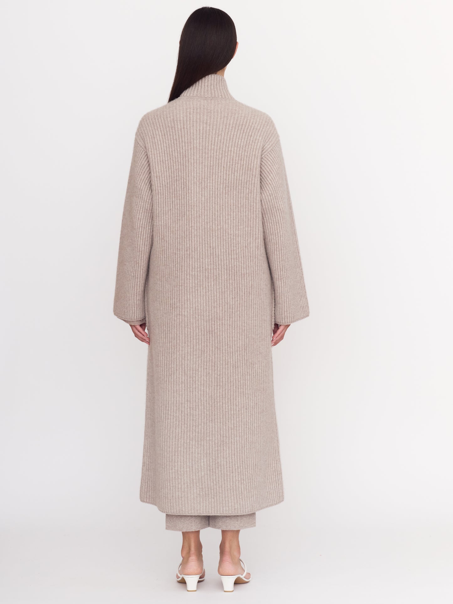 Back view of model wearing cool beige shade of ribbed cashmere knit long coat with long sleeves.