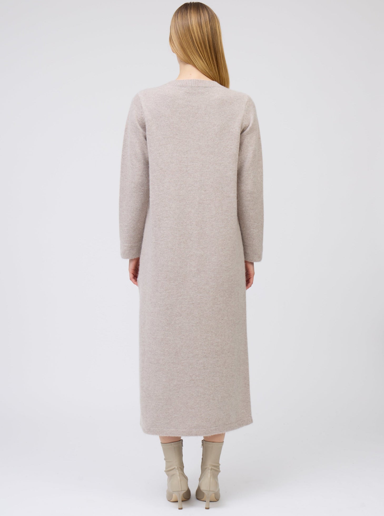 Back view of model wearing plain round neck straight cut maxi dress in beige cashmere, with long sleeves and side slit.