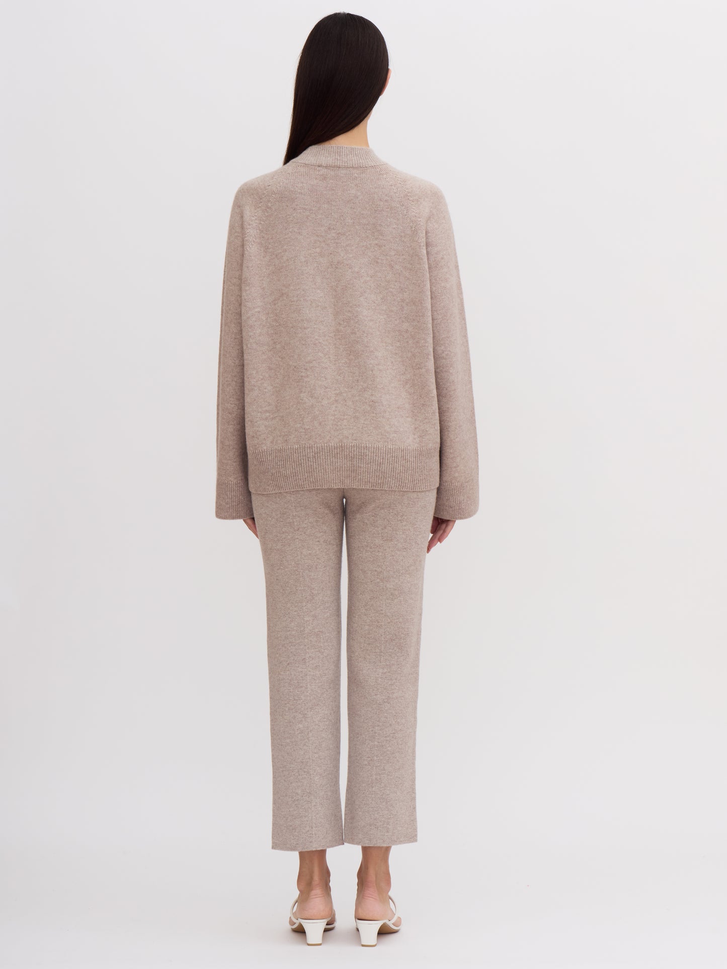 Back view of model wearing beige cashmere outfit: cashmere mock neck jumper and cropped cashmere suit pants.