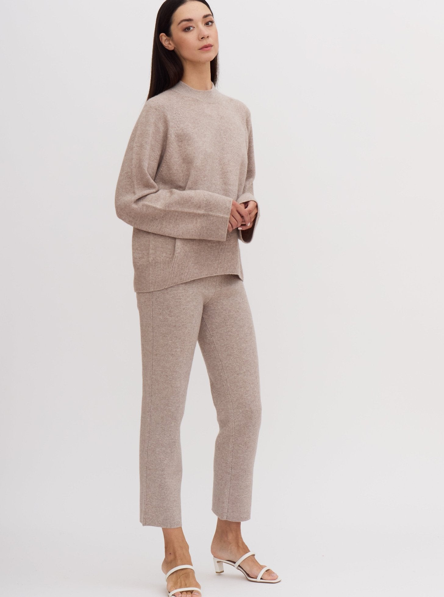 Model wearing beige cashmere outfit: cashmere mock neck jumper with wide sleeves with matching cropped suit pants.