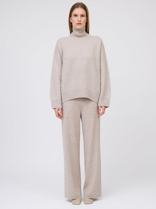 Front view of model wearing beige cashmere oversized roll neck jumper; worn with beige wide leg trousers.