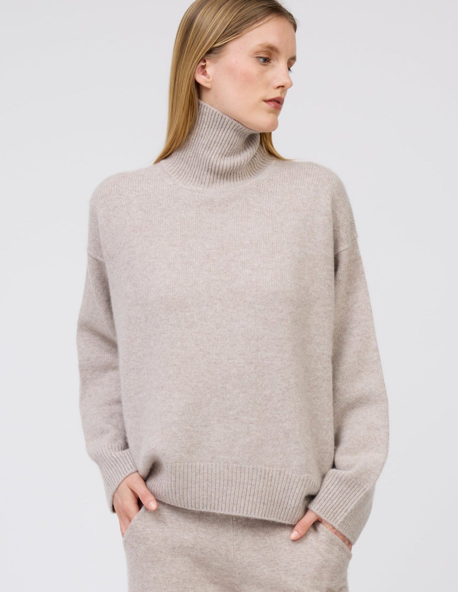 Close-up of model wearing cool beige cashmere oversized roll neck jumper with generous long sleeves.