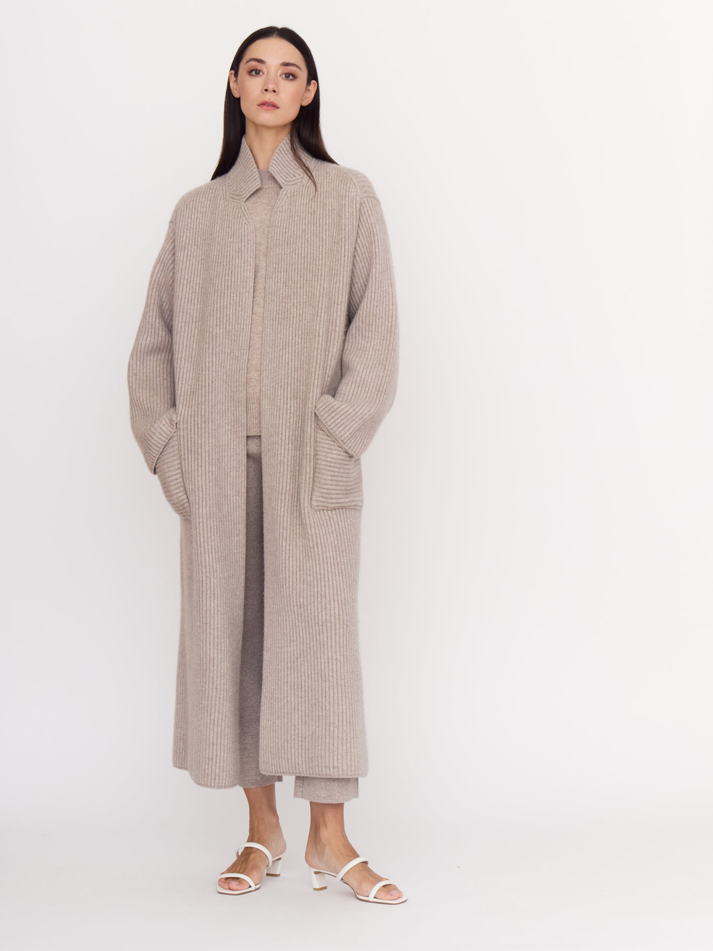Model wearing cool beige shade of ribbed cashmere knit long coat with hands in deep patch pockets.