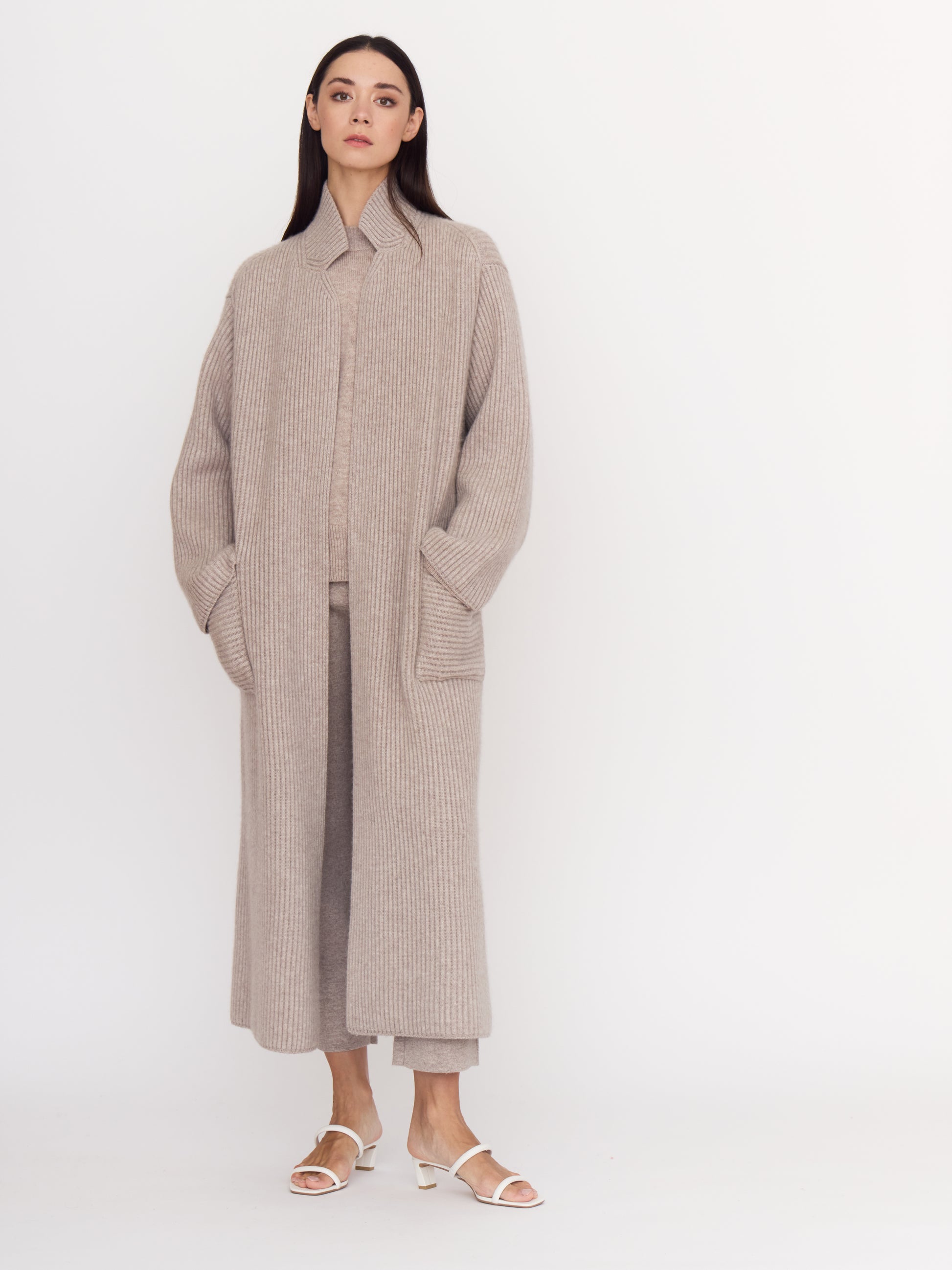 Model wearing cool beige shade of ribbed cashmere knit long coat with hands in deep patch pockets.