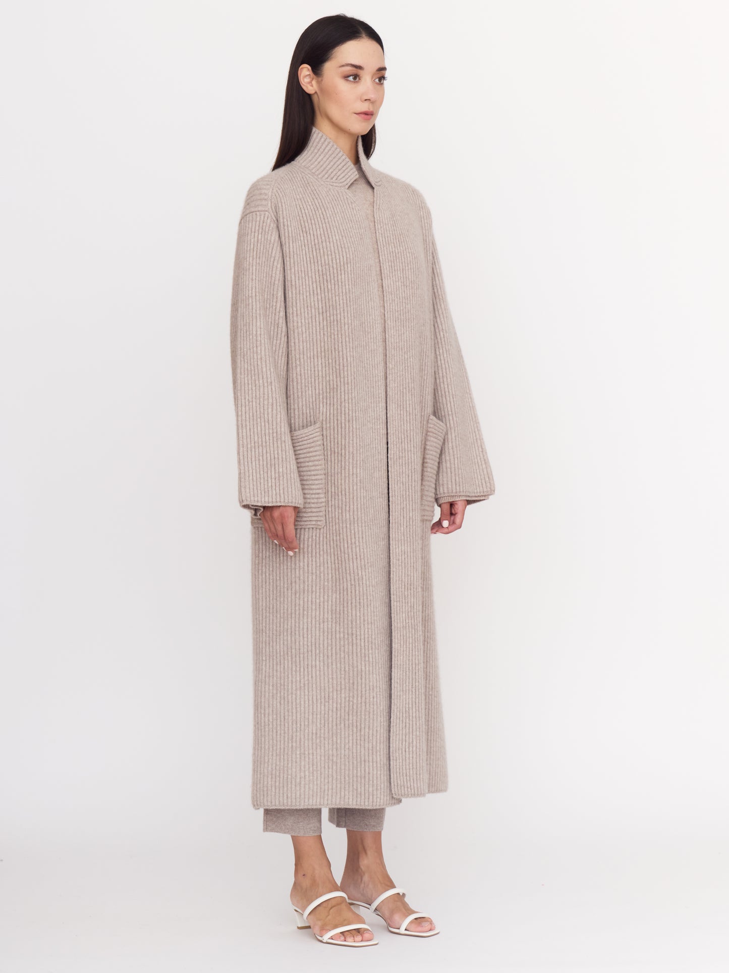 Model wearing cool new beige shade of ribbed cashmere knit long coat with long sleeves and patch pockets.