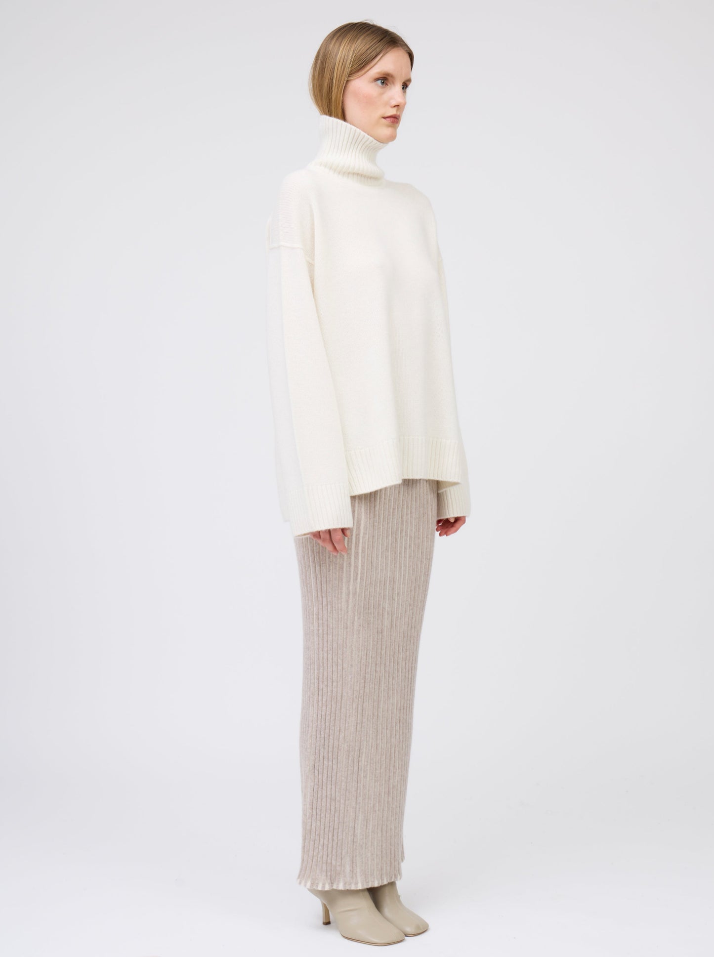 Side view model wears maxi length slim tube skirt in beige and white vertical stripes; worn with oversized natural white roll neck cashmere jumper.