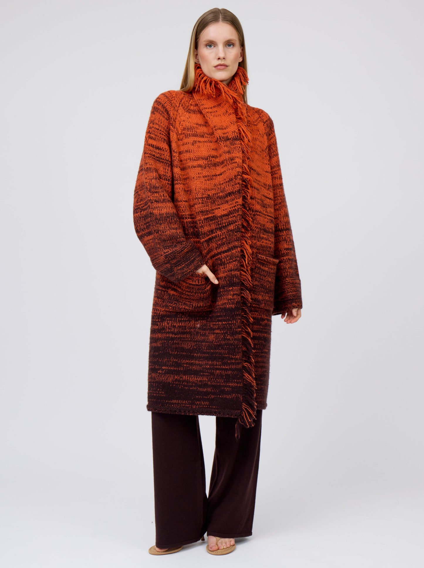 Front view model wearing orange/black mix knit cashmere coat with fringed collar turned up; worn with brown pants.