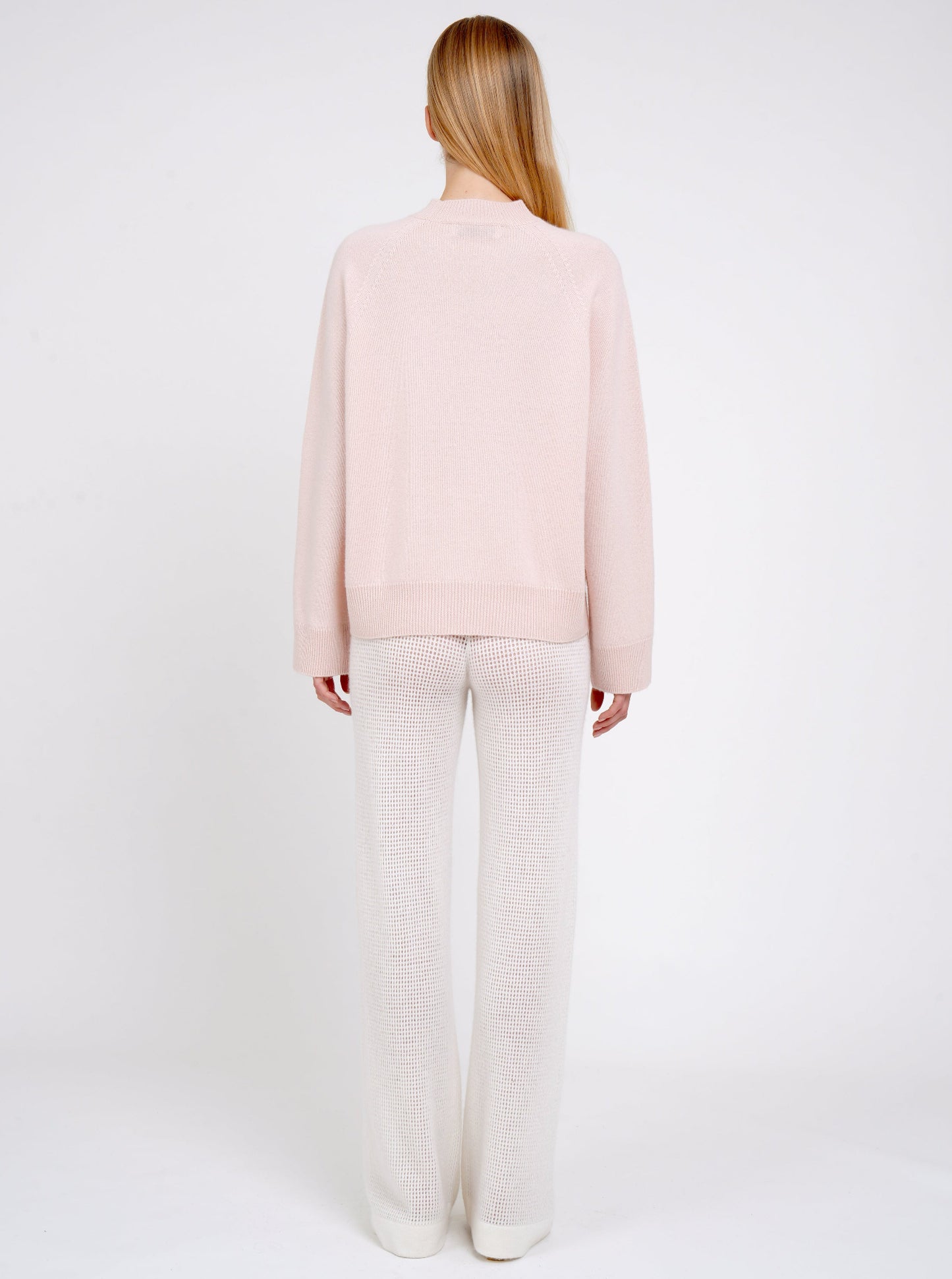 Back view model in peach cashmere jumper with round neck, long sleeves and white net knit wide leg pants