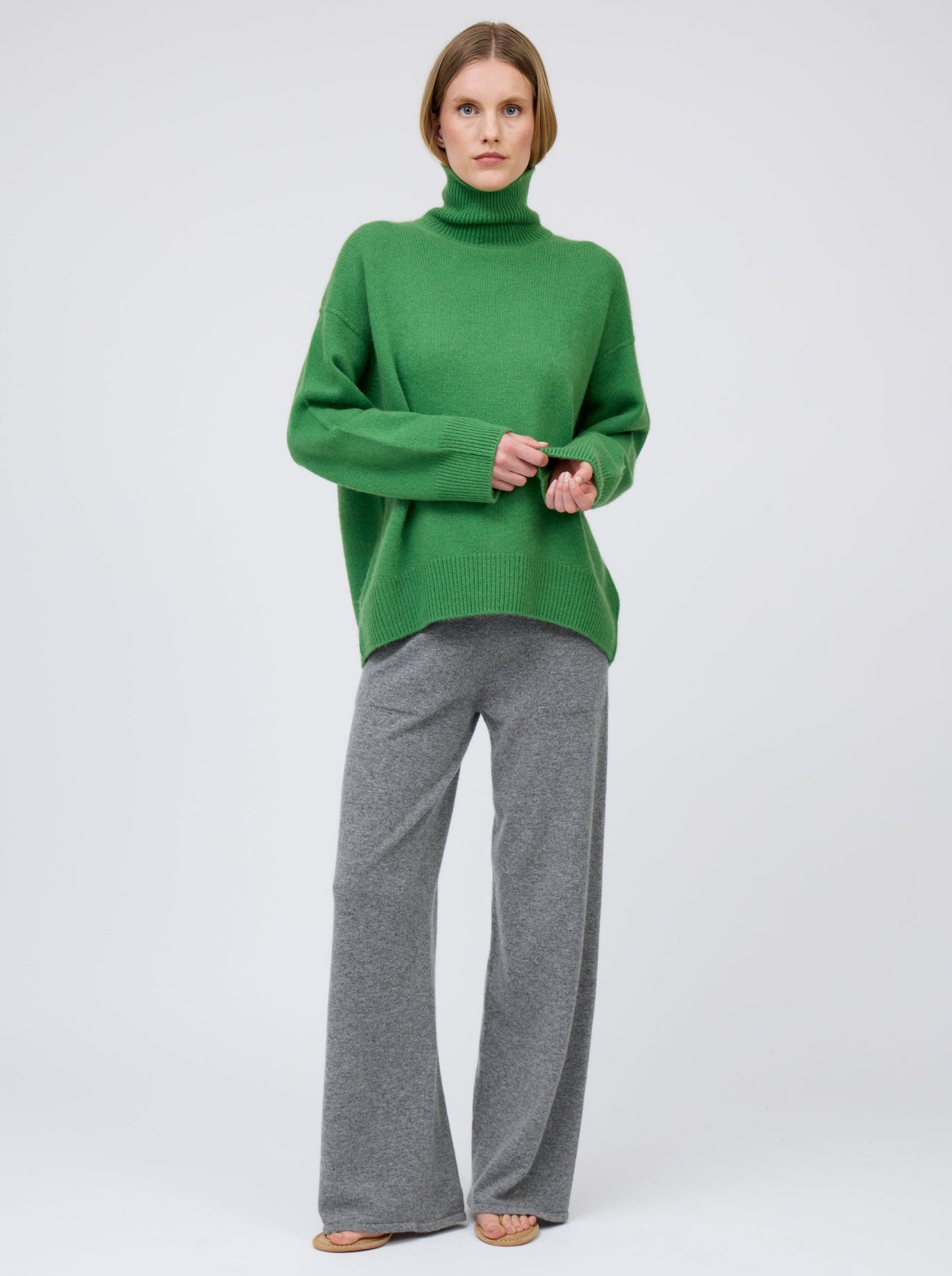Front view, relaxed pose, model wears pine green cashmere roll neck oversized jumper with grey cashmere wide leg pants.