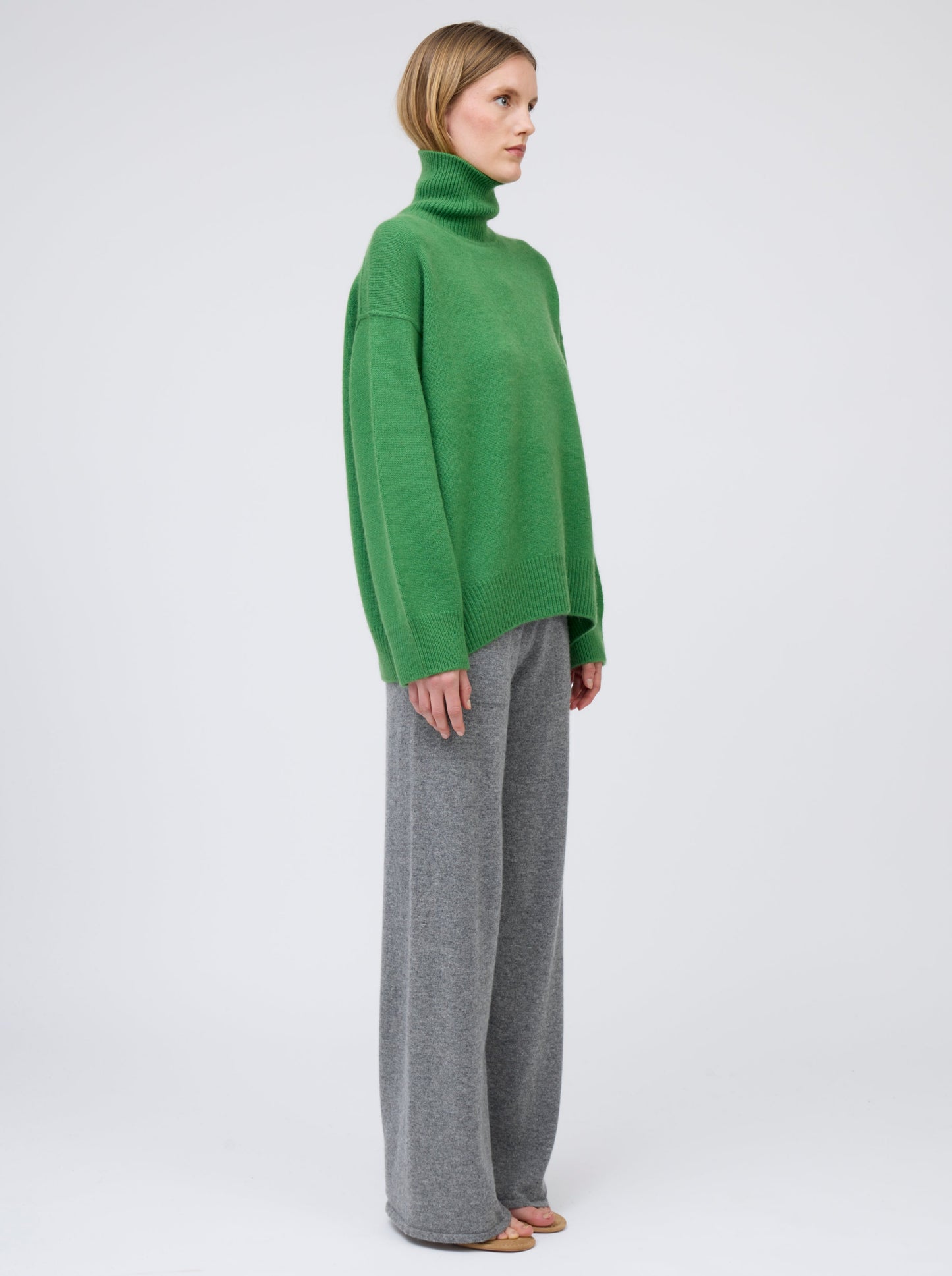 Side view model wears pine green cashmere roll neck oversized jumper with grey cashmere wide leg pants.