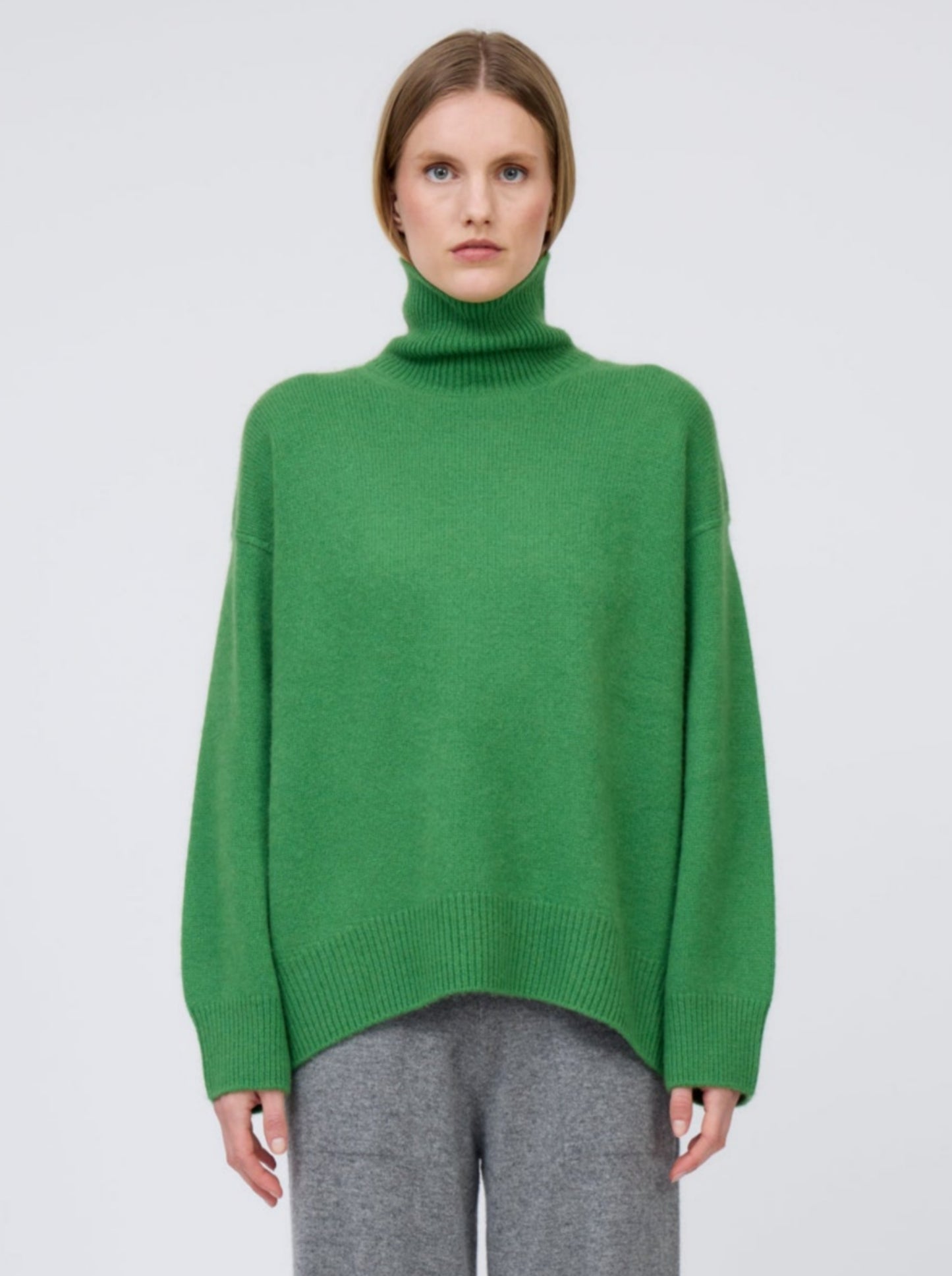 Straight on, front view model wears pine green cashmere roll neck oversized jumper with grey cashmere wide leg pants.