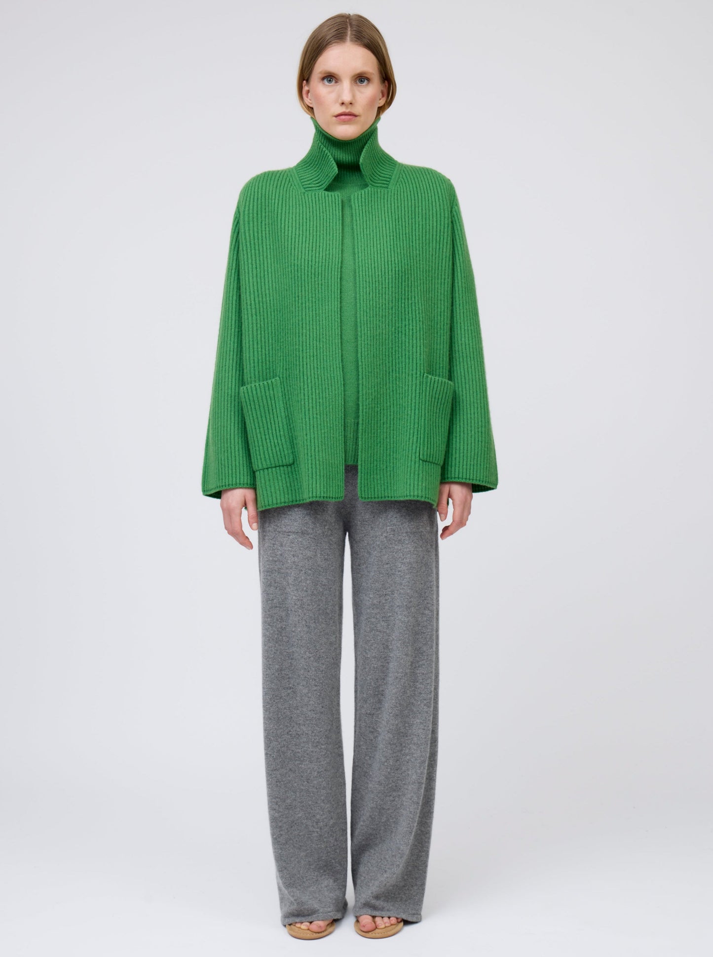 Model wears pine green ribbed knit cashmere hip-length jacket with high collar, wide sleeves and patch pockets; worn with grey wide leg pants.