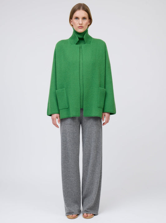 Model wears pine green ribbed knit cashmere hip-length jacket with high collar, wide sleeves and patch pockets; worn with grey wide leg pants.