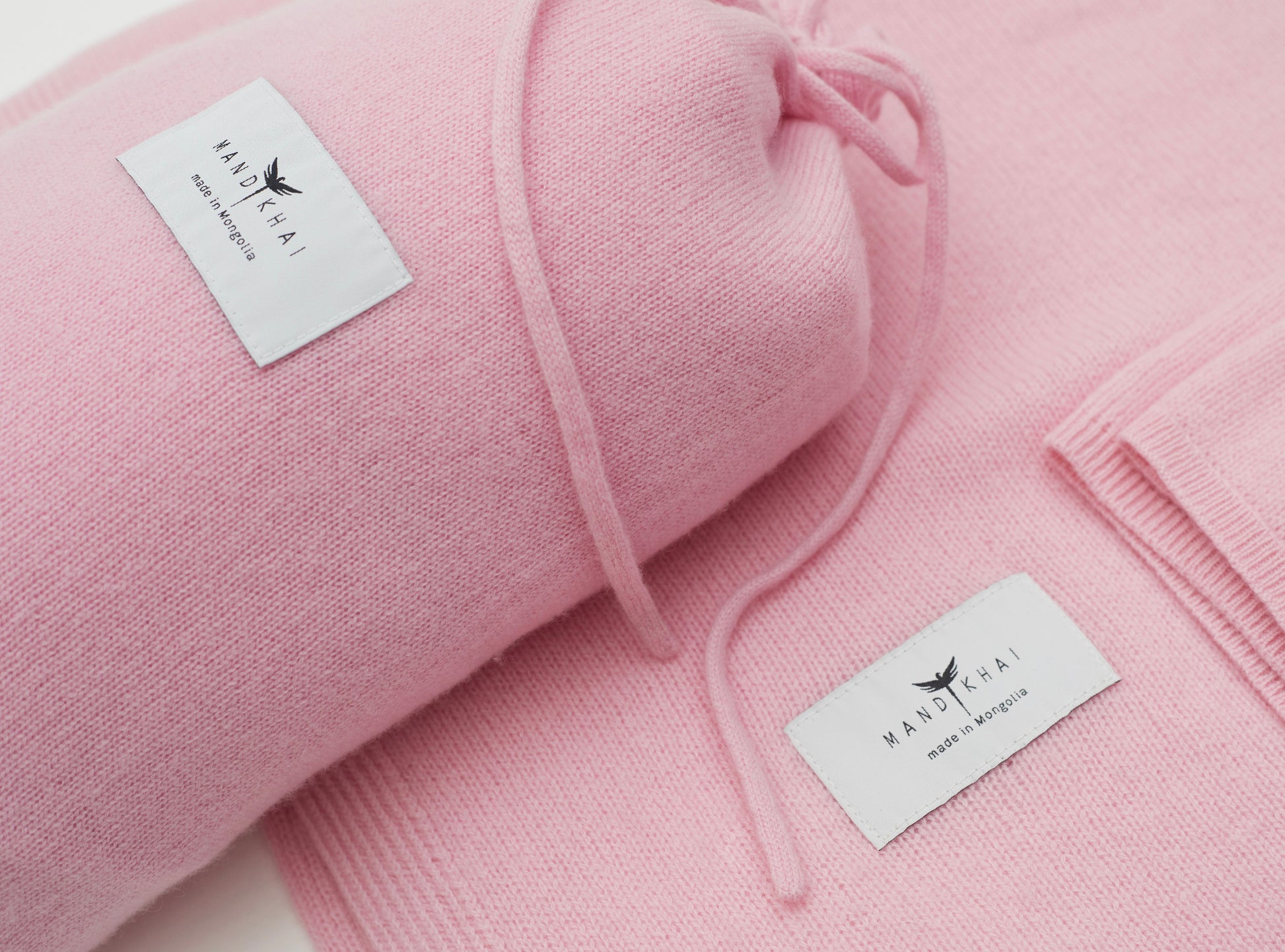 Close up flat lay of the Pink Cashmere Shawl With Travel Pouch featuring Mandkhai's label and the side of the travel pouch
