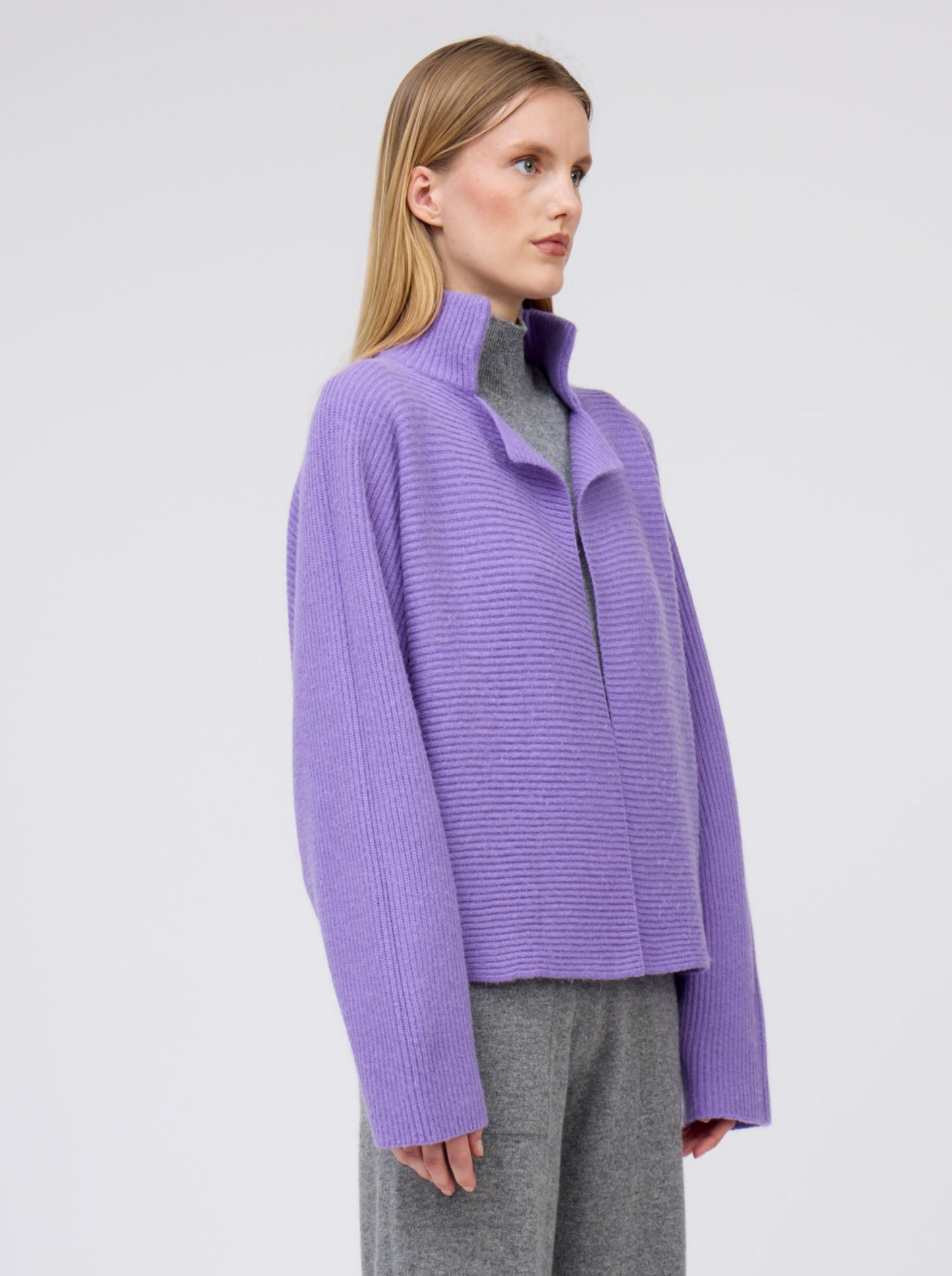 Close-up model in purple cashmere ribbed knit jacket with kimono sleeves and high collar; worn with grey cashmere wide leg pants.
