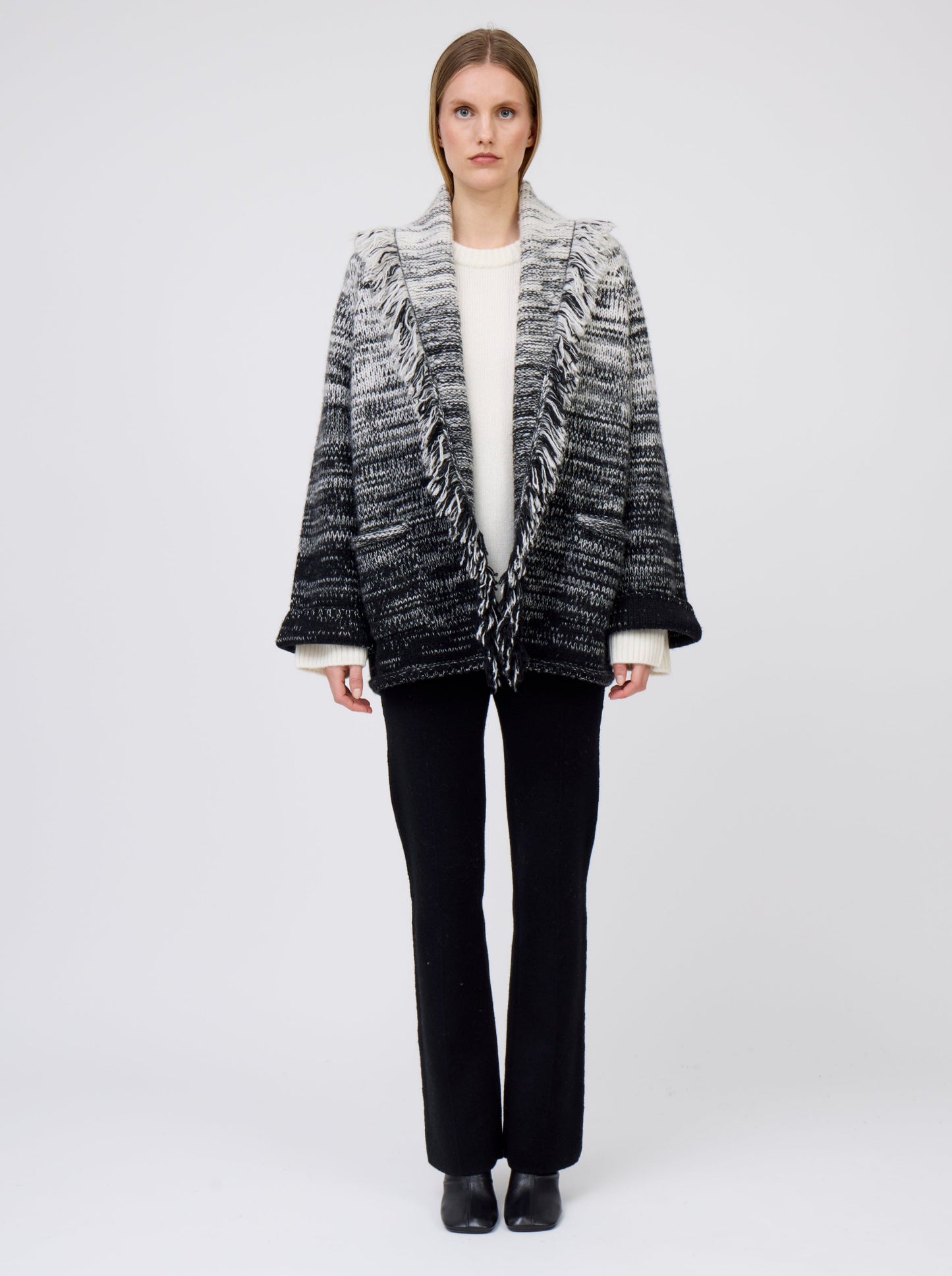 Model wears gradient colour mix knitted cashmere jacket in white and black over white cashmere sweater and black suit pants.