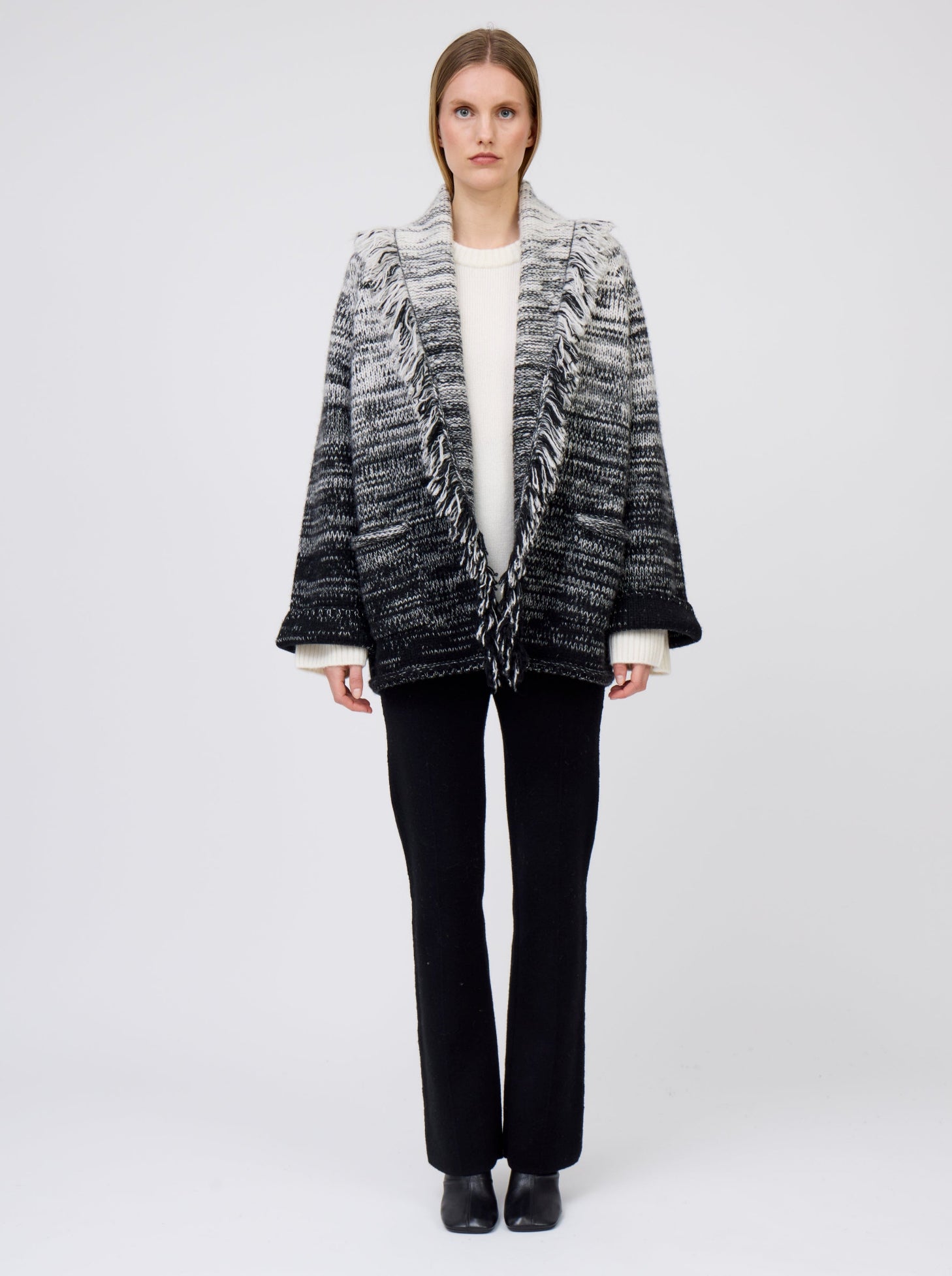 Model wears  gradient colour mix knitted cashmere jacket in white and black over white cashmere sweater and  black suit pants.