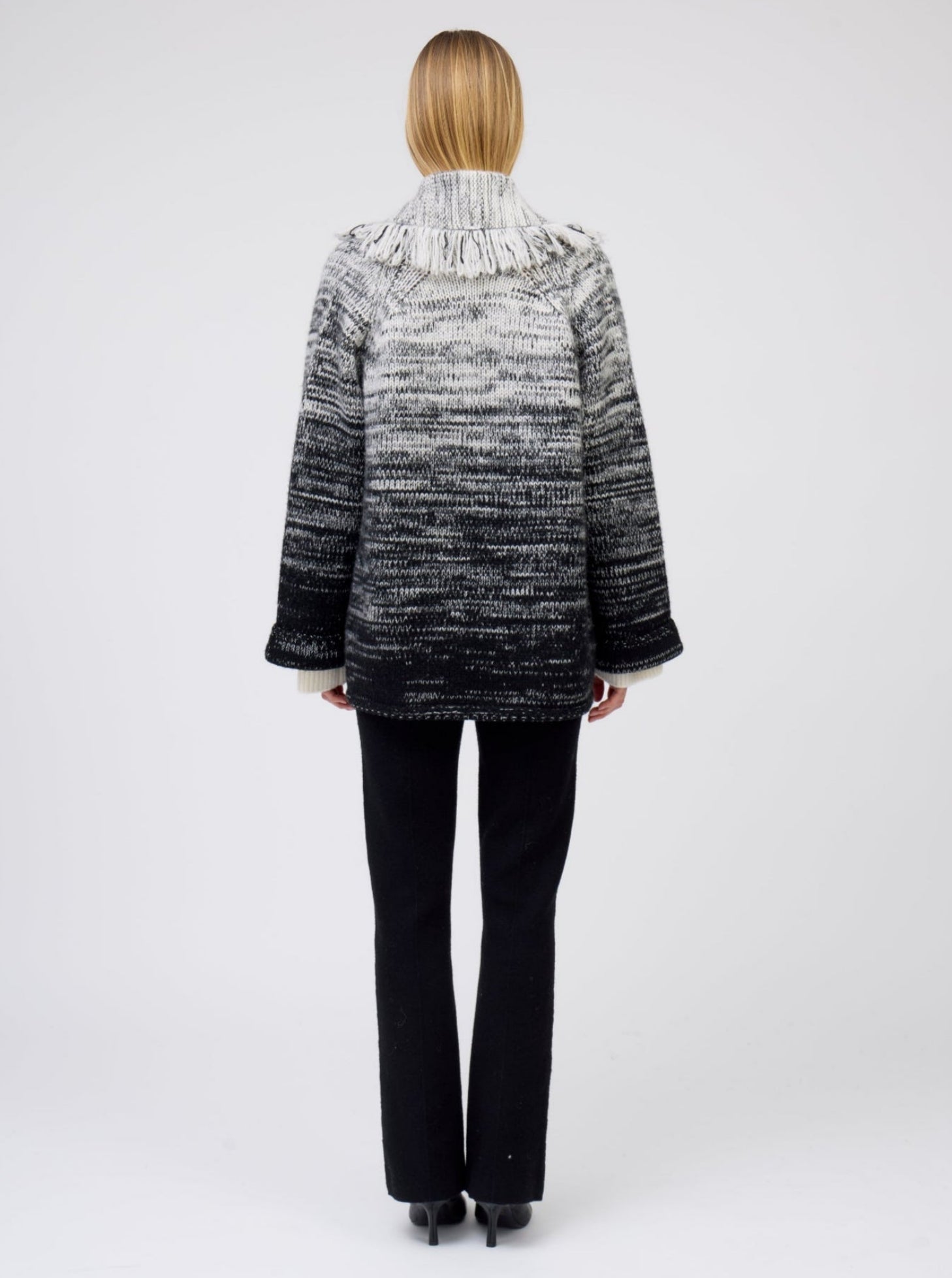 Back view of model wearing gradient colour mix knitted cashmere jacket  with shawl collar in white and black over black cashmere suit pants.