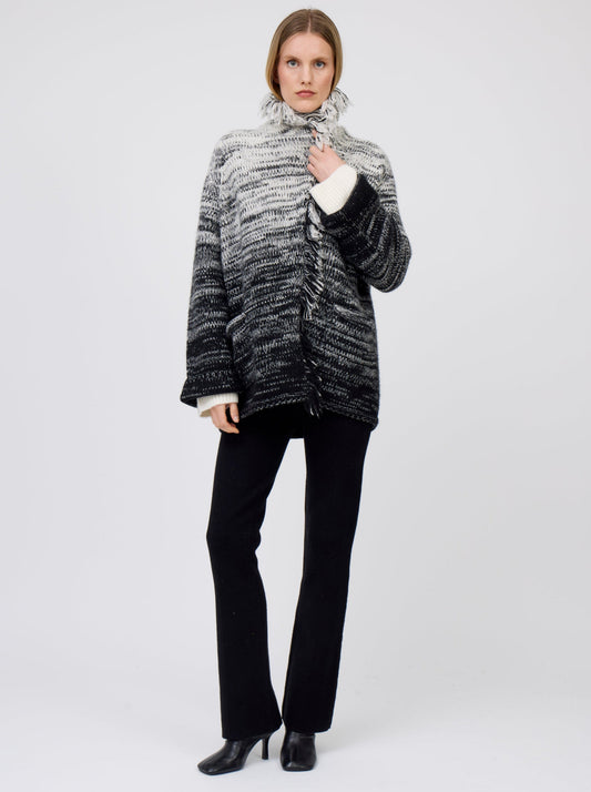 Model wears white and black colour mix knitted cashmere jacket with fringe collar turned up over black suit pants.