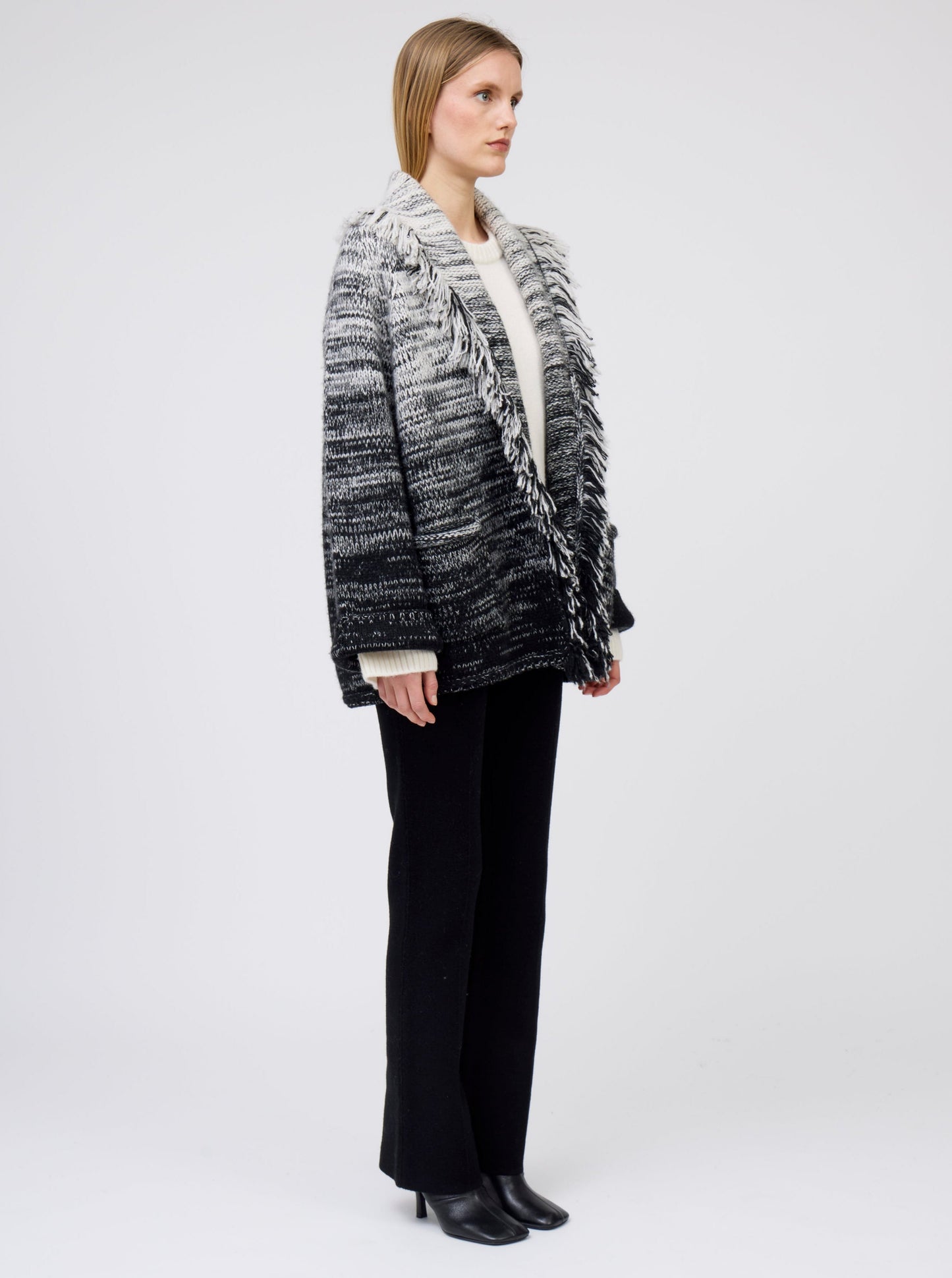 Side view of model wearing gradient colour mix knitted cashmere jacket in white and black over white cashmere sweater and black cashmere suit pants.