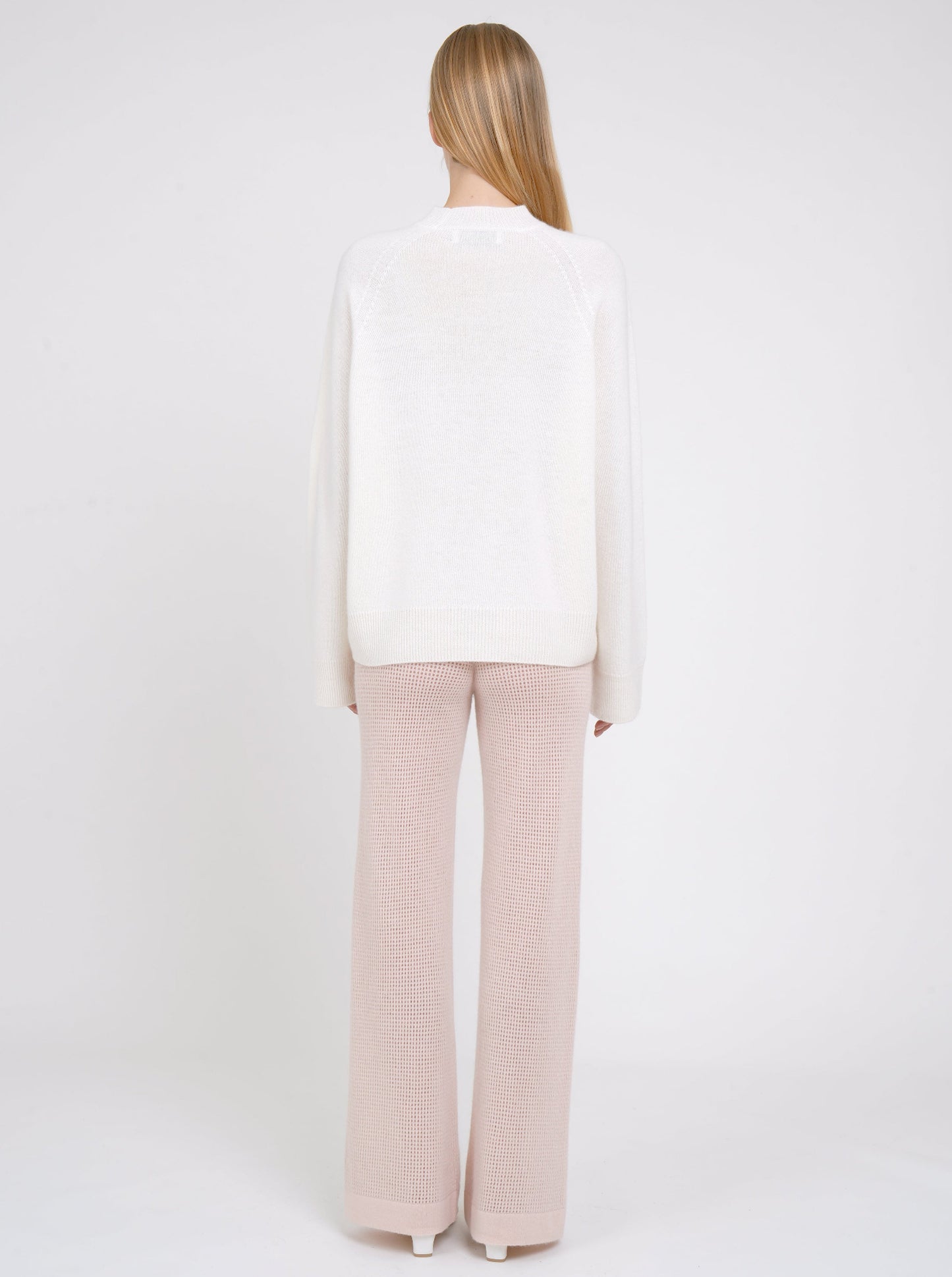 Back view model in white cashmere jumper with round neck, long sleeves and pale peach pink knit cashmere pants.