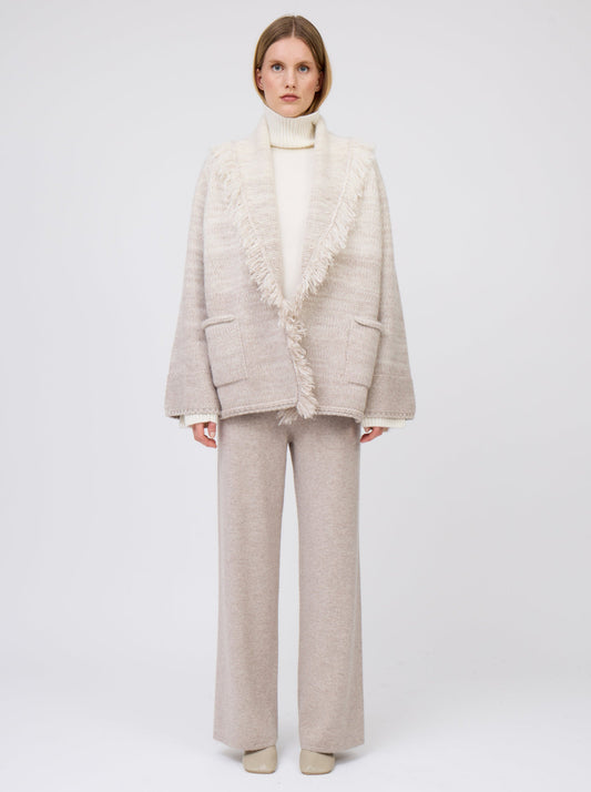 Model wears  gradient colour mix knitted cashmere jacket in white and pale beige over white cashmere roll neck sweater and beige wide leg cashmere pants.
