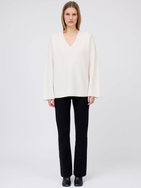Front view of model wearing creamy white V-neck ribbed knit cashmere jumper with black suit pants and black boots.