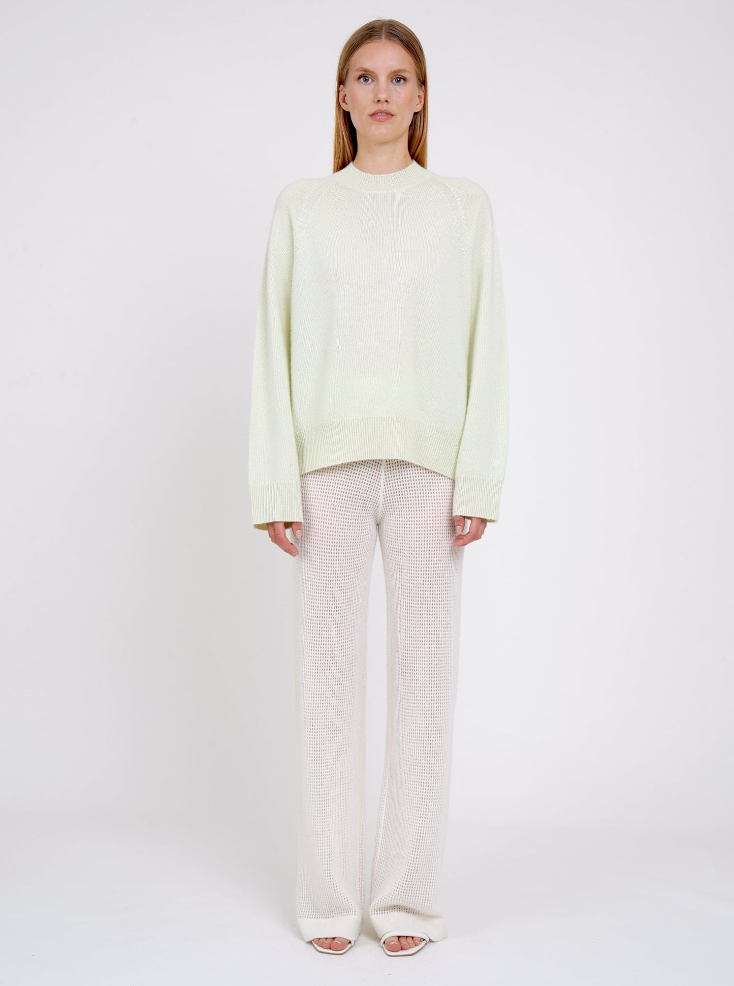 Model wearing a light green sweater and white pants on a white background