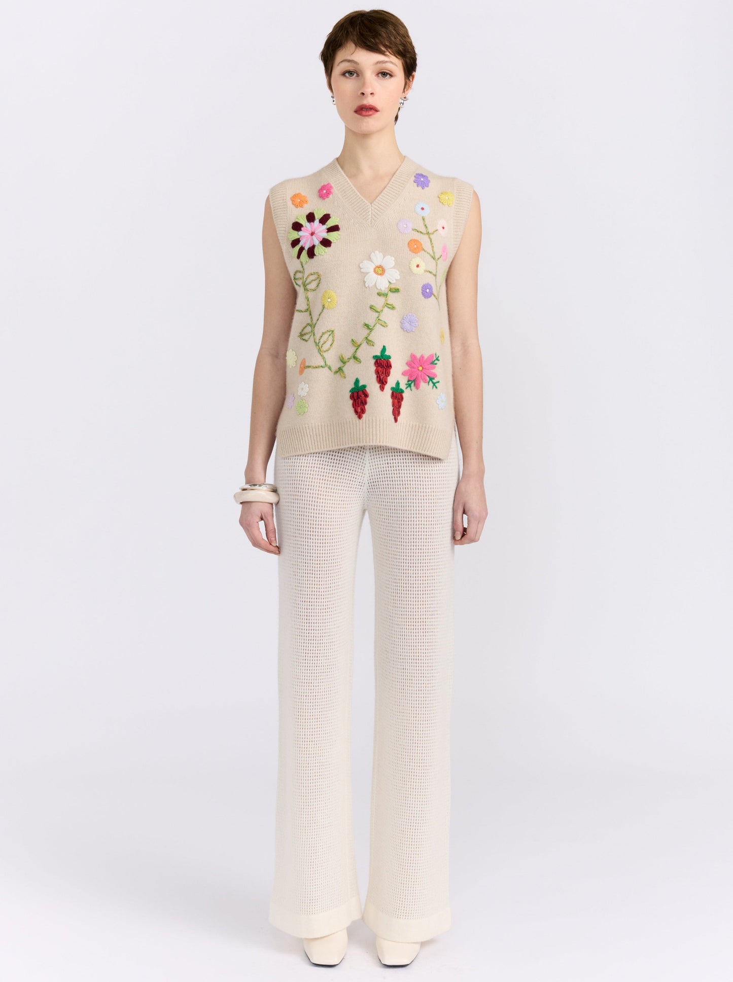 Beige cashmere vest with hand-embroidered floral detailing, styled with black wide-leg trousers.