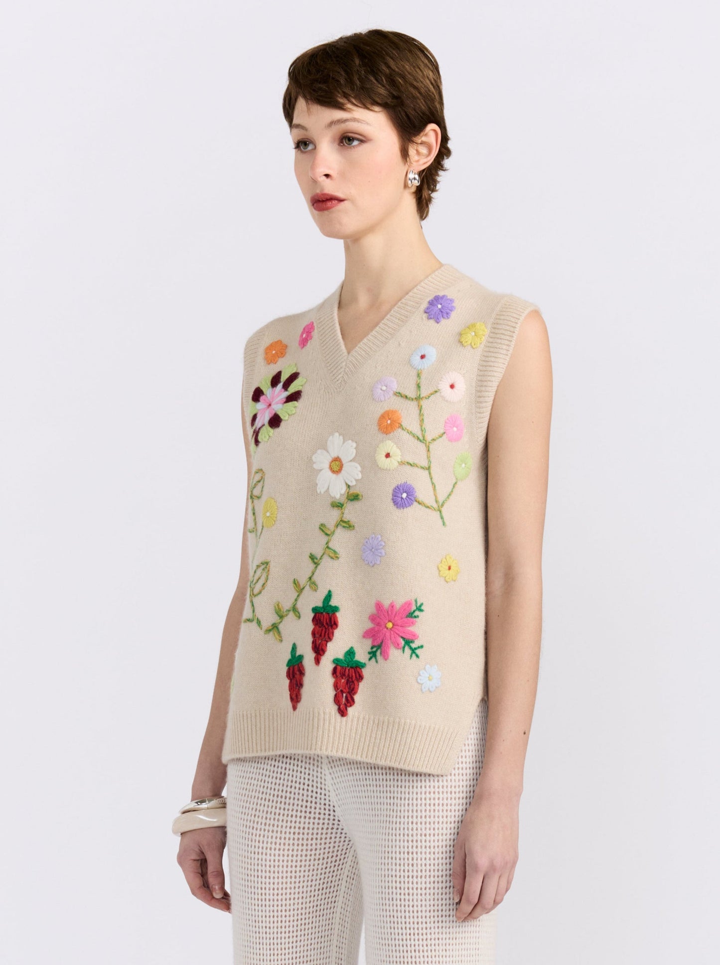 Beige cashmere vest with hand-embroidered floral detailing, styled with black wide-leg trousers.
