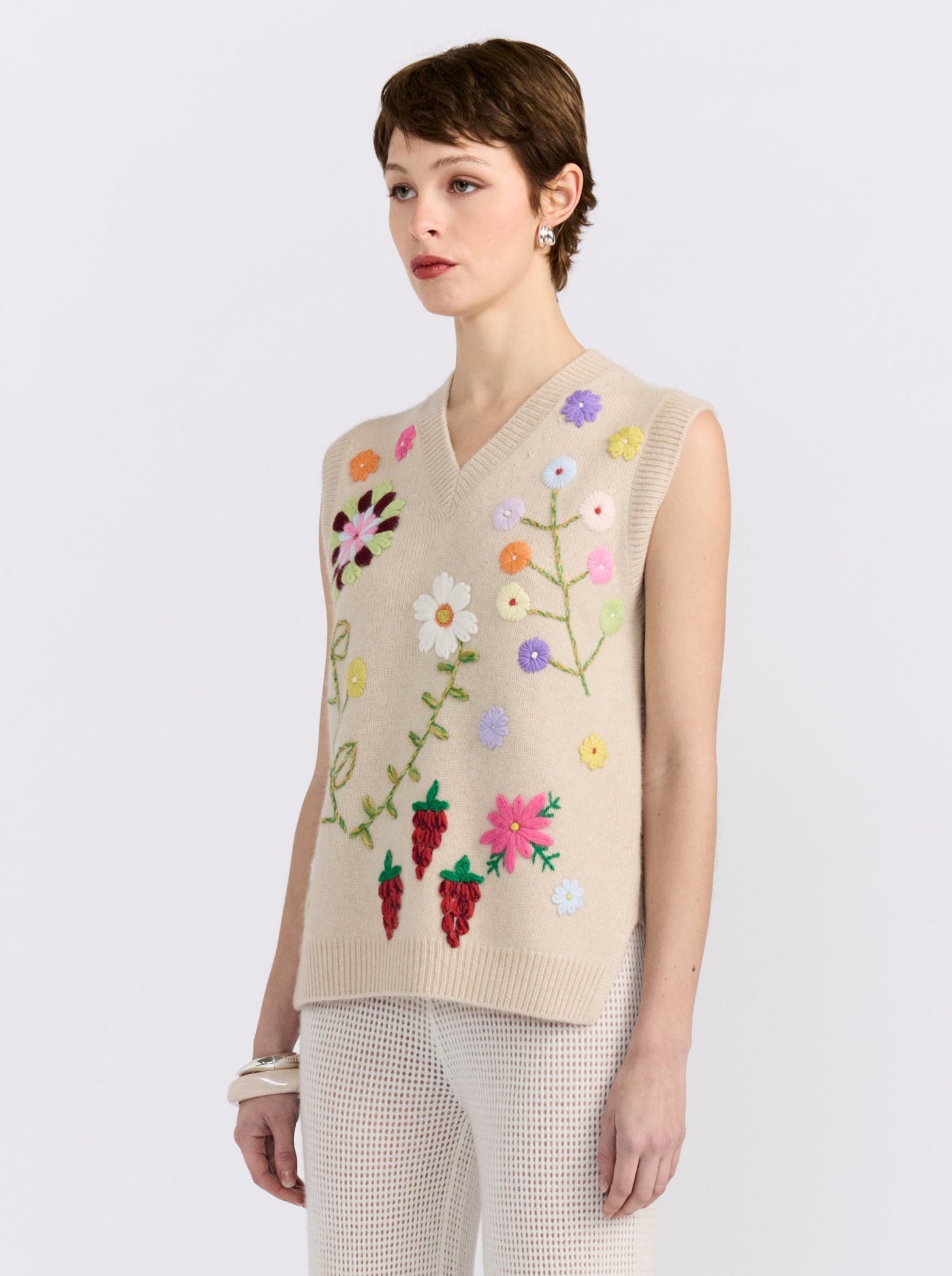 Beige cashmere vest with hand-embroidered floral detailing, styled with black wide-leg trousers.